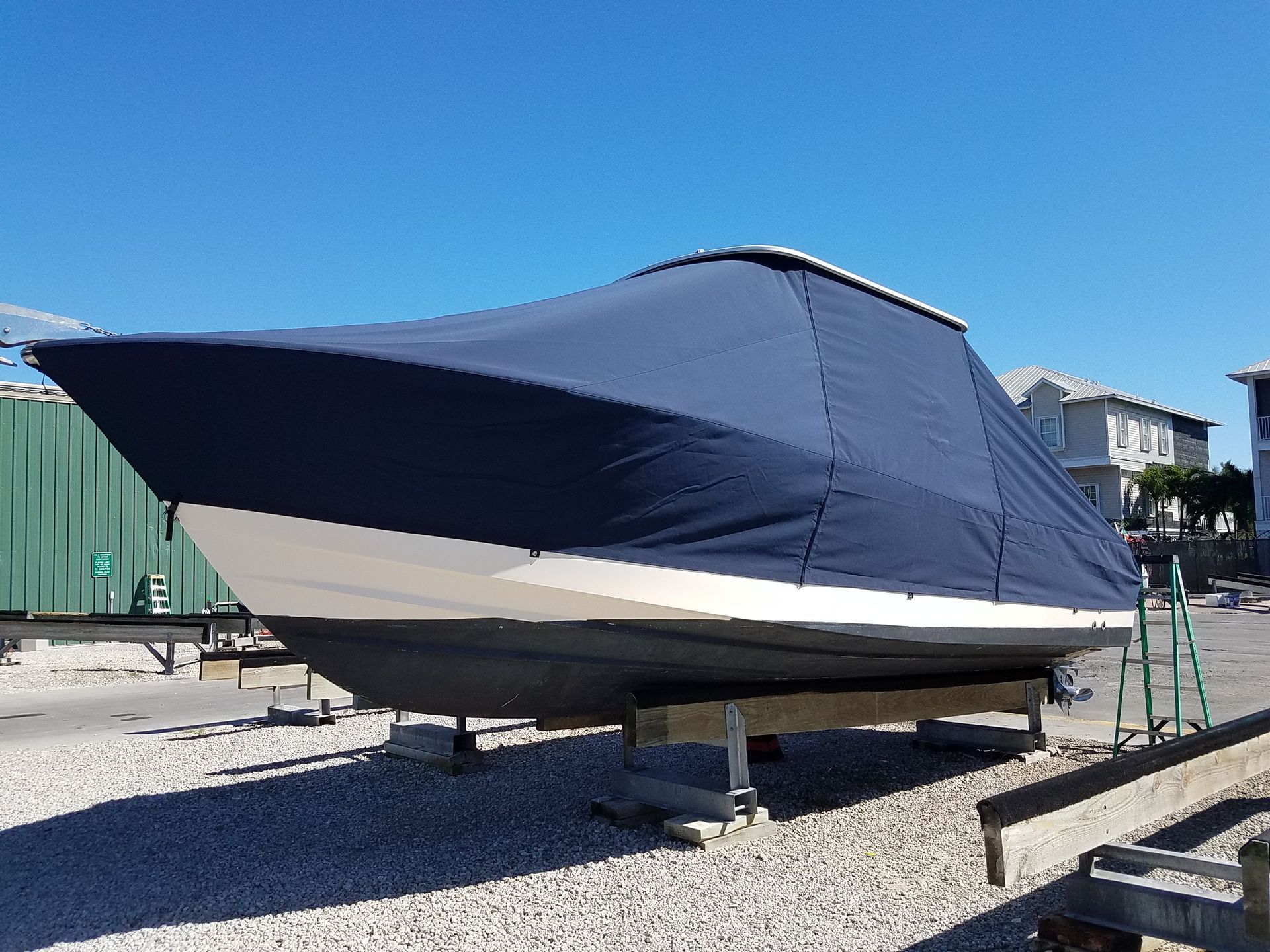 A boat with a blue cover on it is sitting on gravel