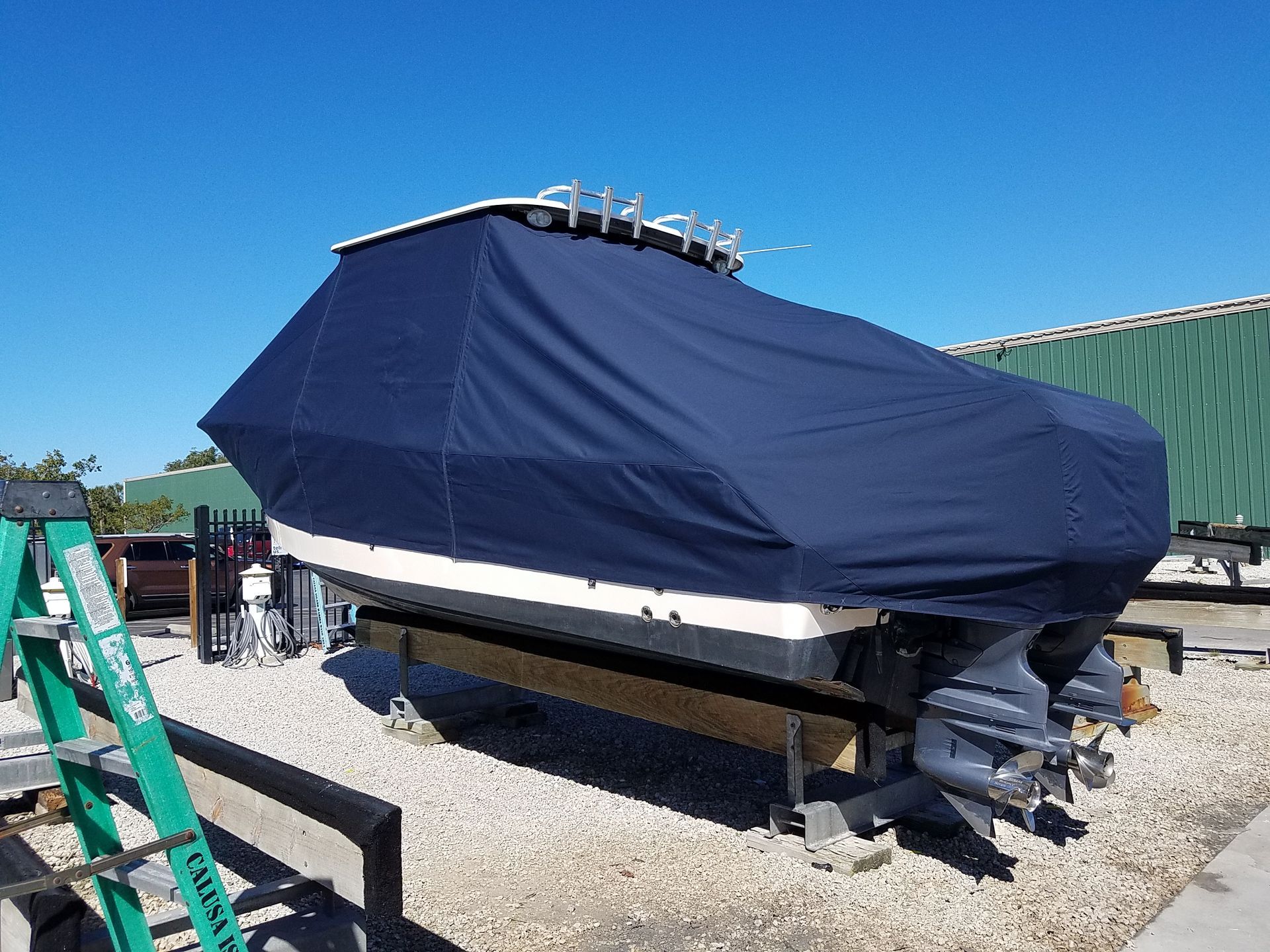 A boat with a cover on it is sitting on top of a gravel lot.