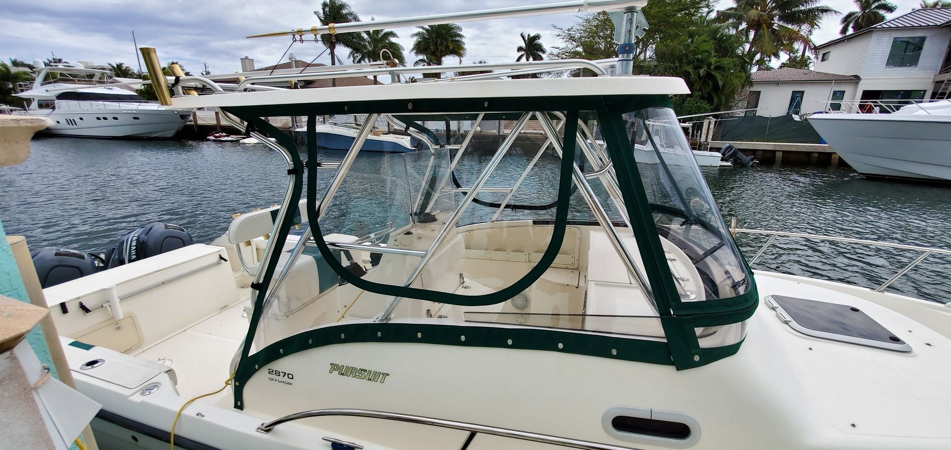A white boat with a green canopy is docked in a marina.