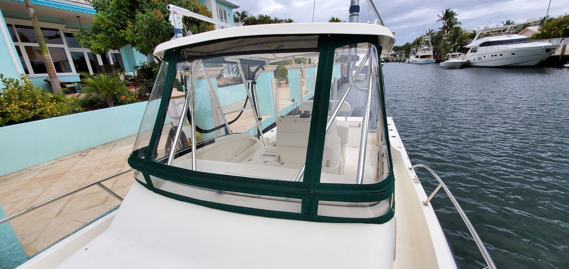 A white boat with a green windshield is docked in a harbor.