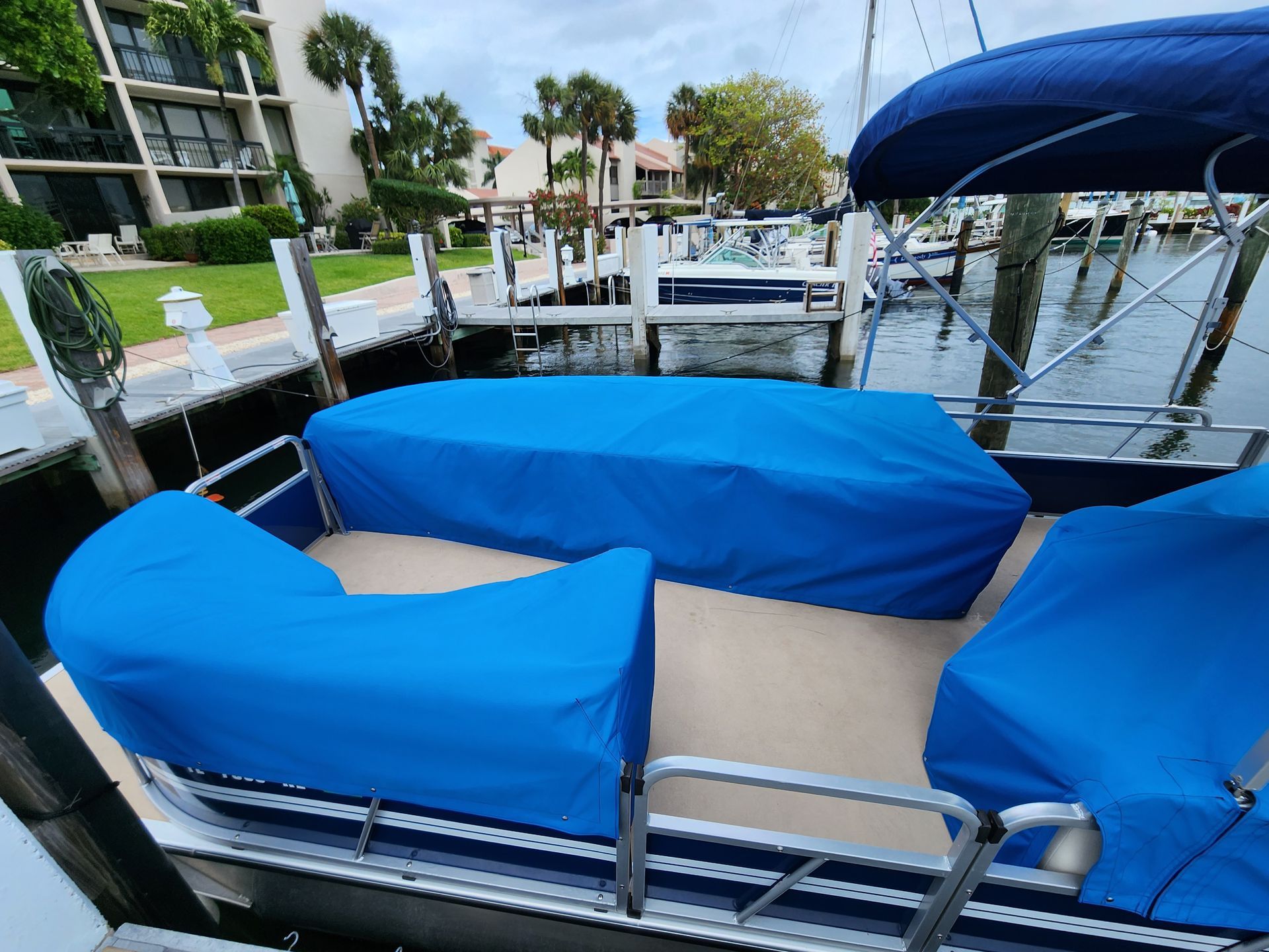 A pontoon boat with a blue cover is docked at a dock.