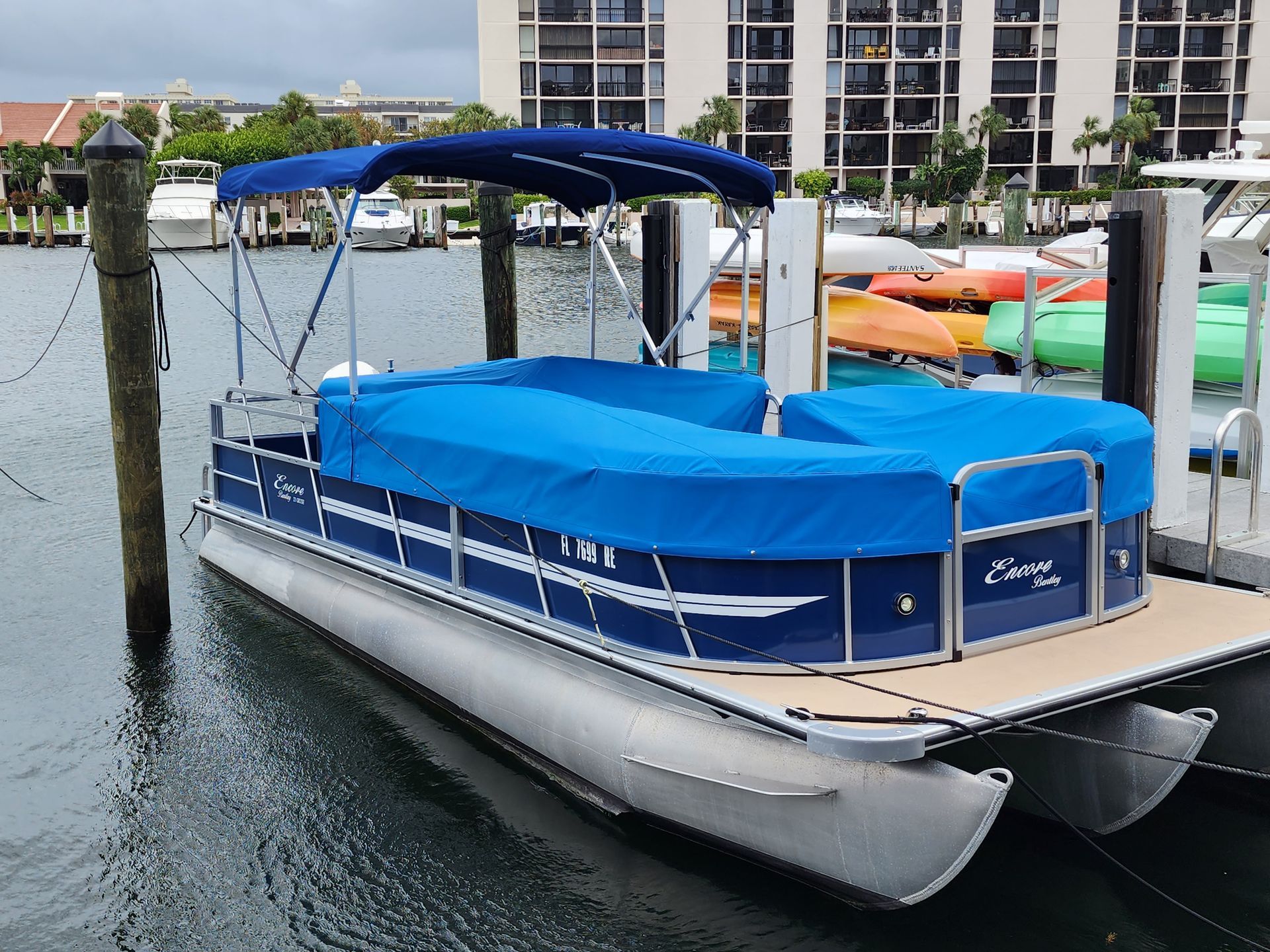 A pontoon boat with a blue cover is docked at a dock