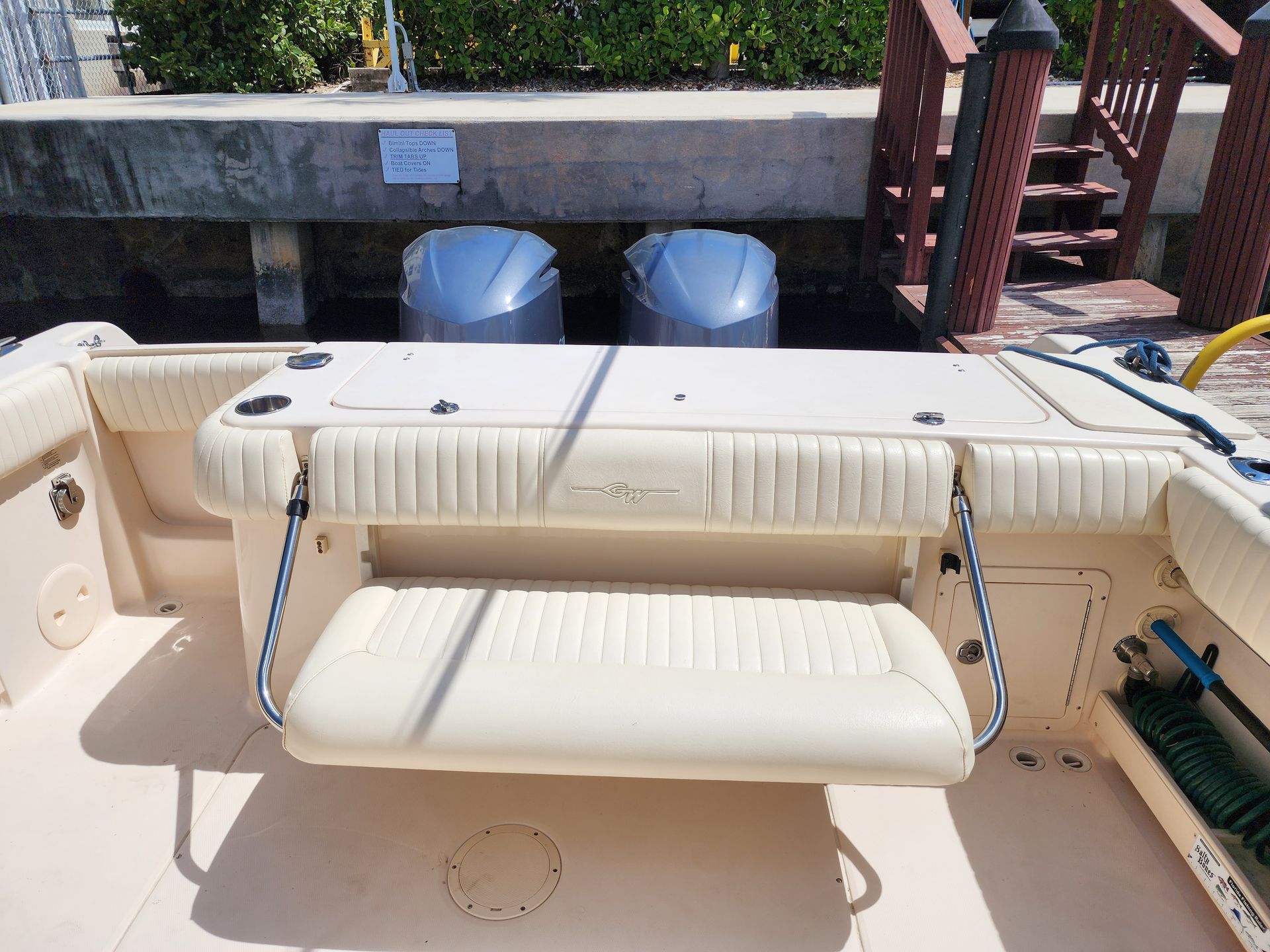 A tan boat with two blue motors docked at a dock. A fold-down seat is visible.