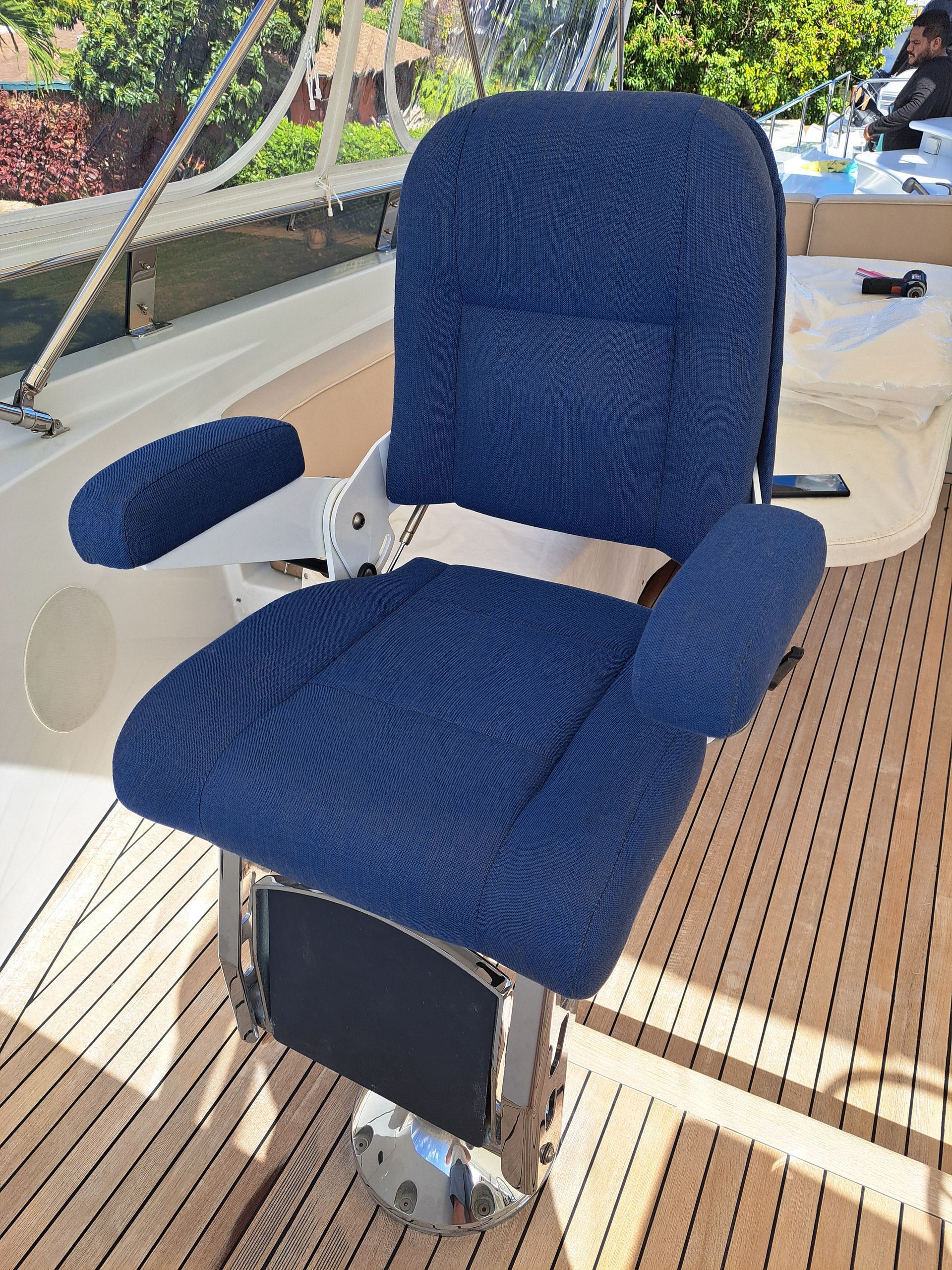 Blue upholstered captain's chair on a boat deck with teak wood, armrests, and silver base.