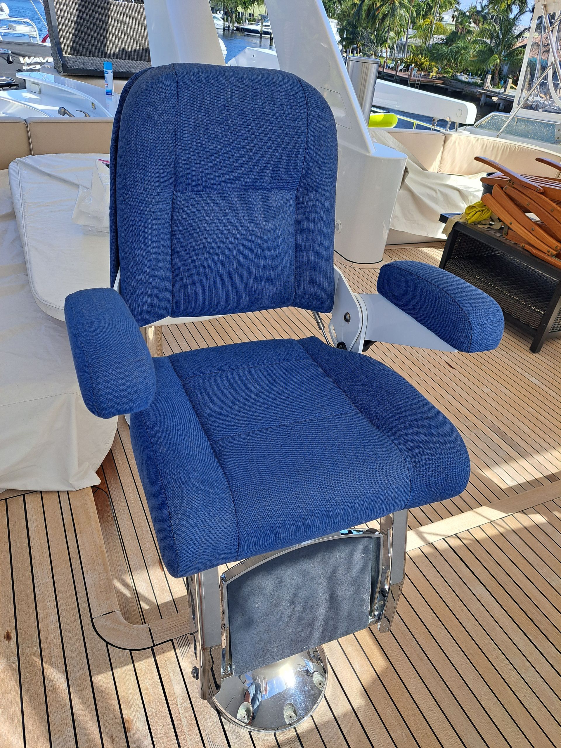 Blue upholstered boat captain's chair on a wooden deck, with chrome base and armrests.