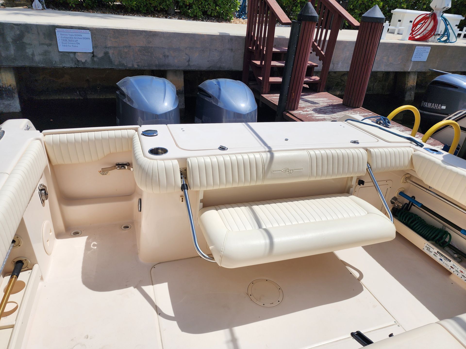 Boat stern with two outboard motors docked at a pier; a flip-down bench is visible.