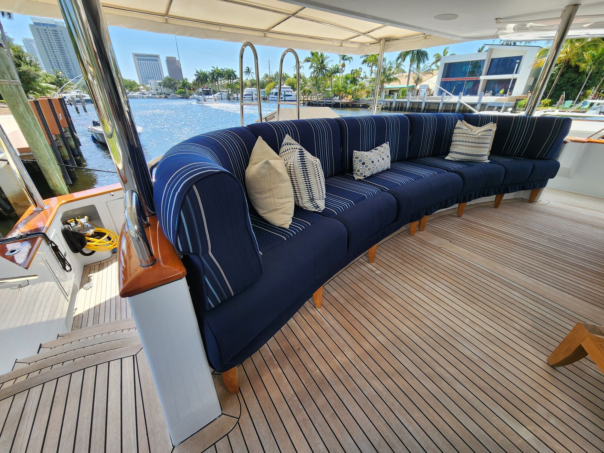 Curved blue couch with pillows on a yacht deck, docked waterfront, sunny day.