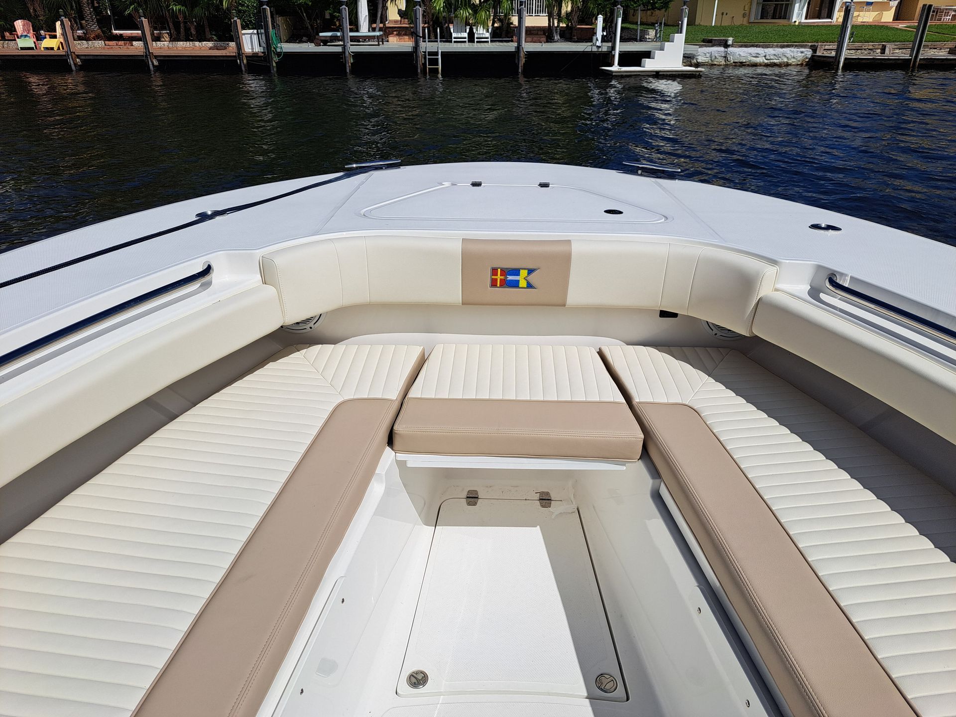 Bow of a boat with beige seats, overlooking a dark waterway and docks under a sunny sky.