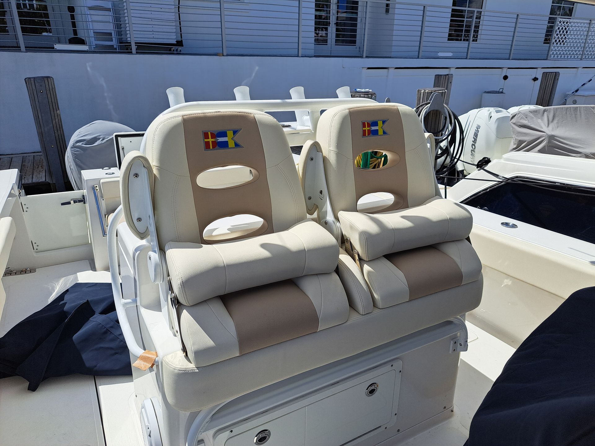 Two beige boat seats with armrests and flags. Outdoors, sunny.
