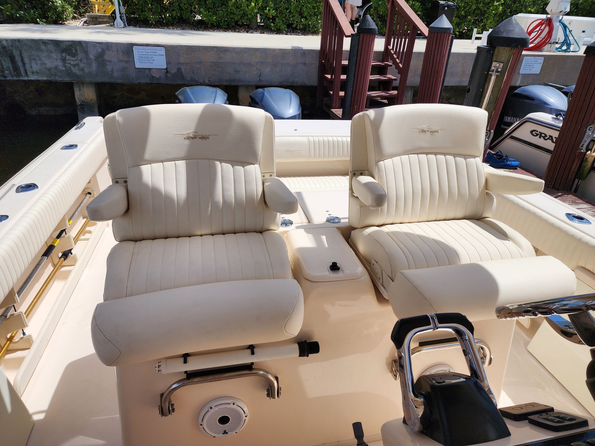 Two cream-colored boat seats with armrests and stitched backrests inside a boat, docked outdoors.