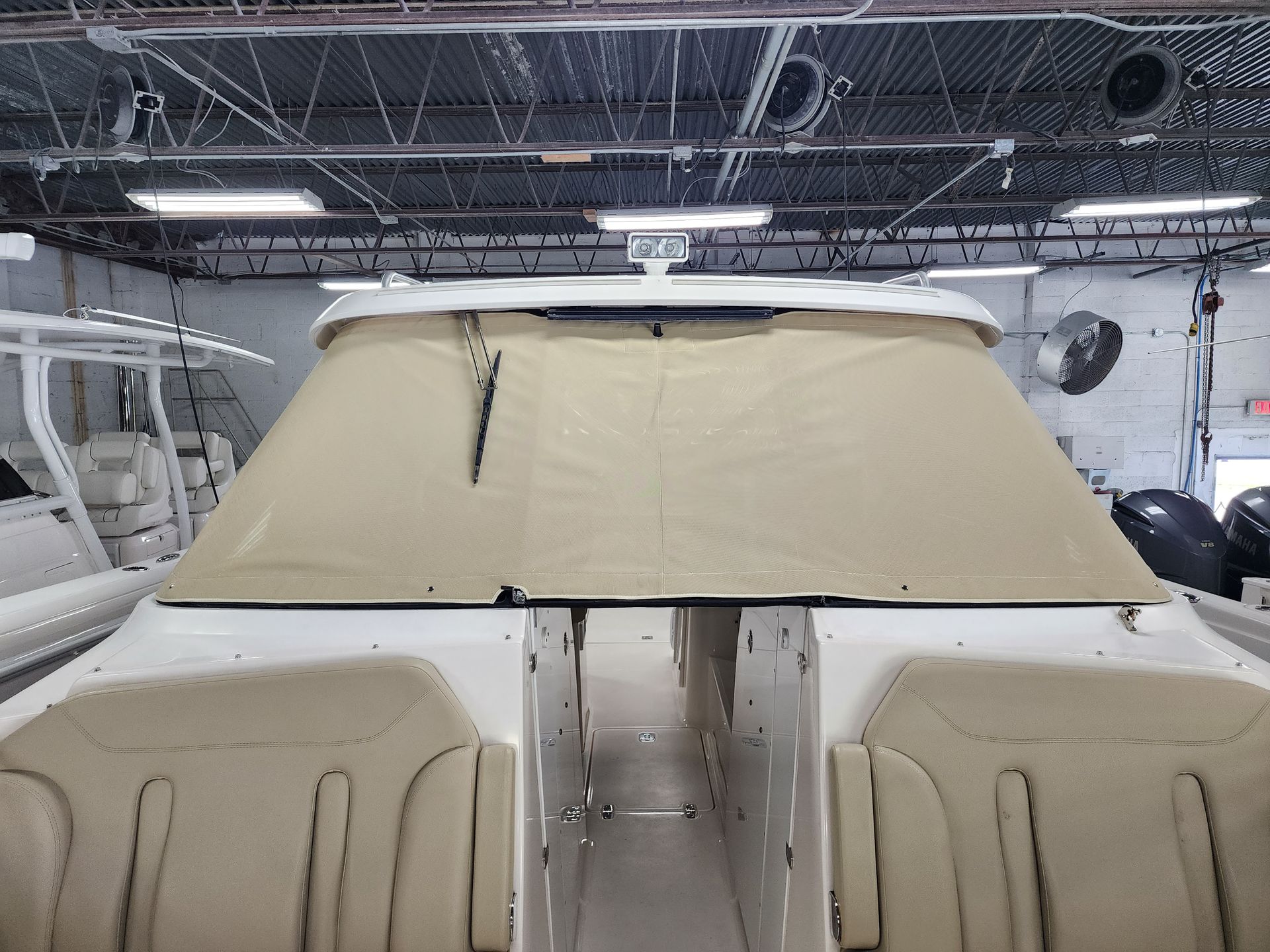 A boat is sitting in a warehouse with a cover on the windshield.