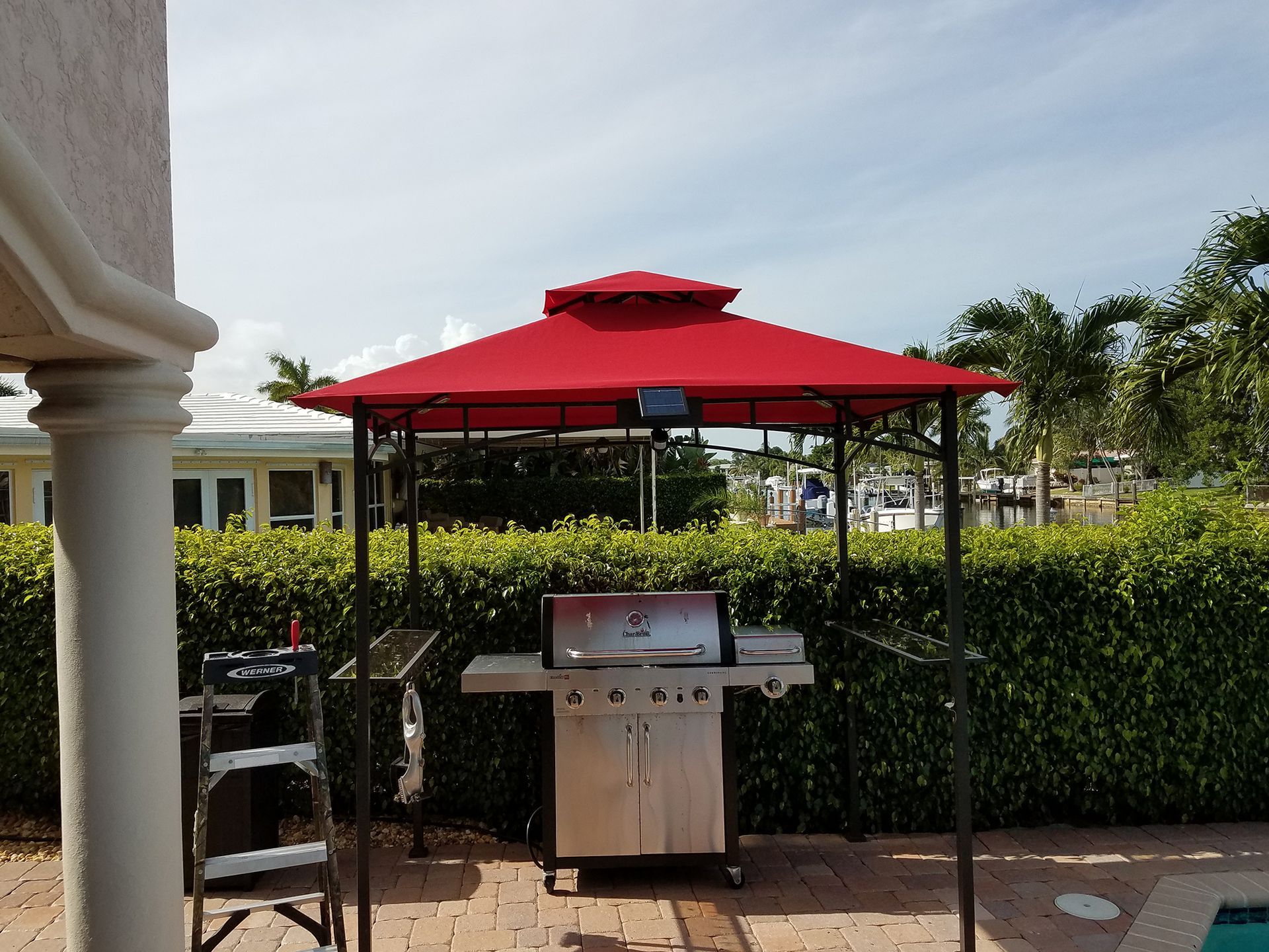 A grill under a red canopy next to a pool