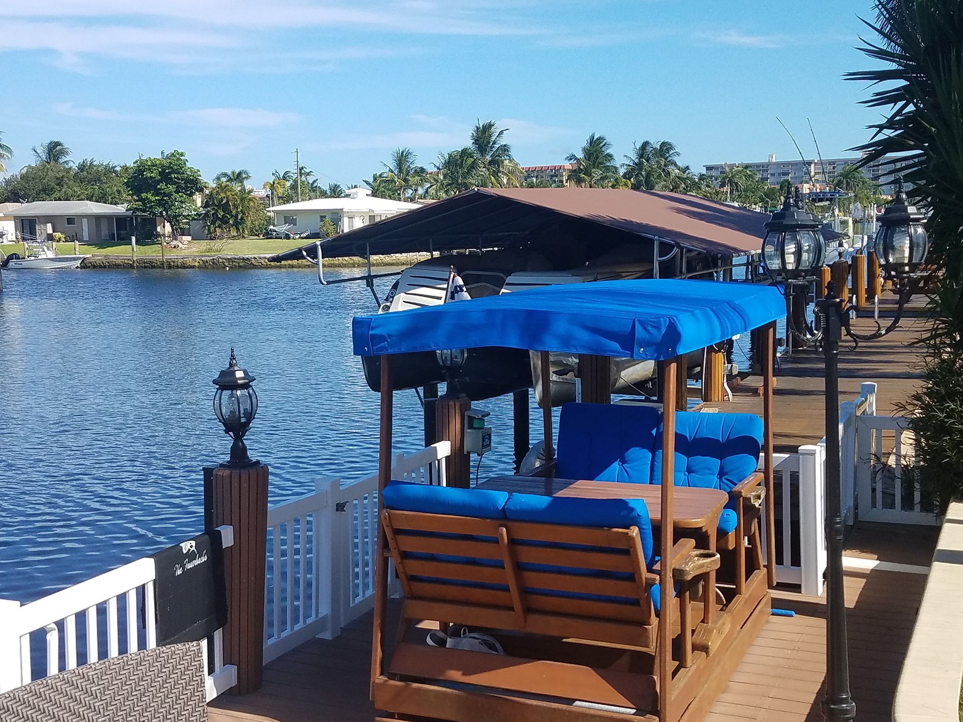 A wooden bench with a blue canopy sits on a dock overlooking a body of water