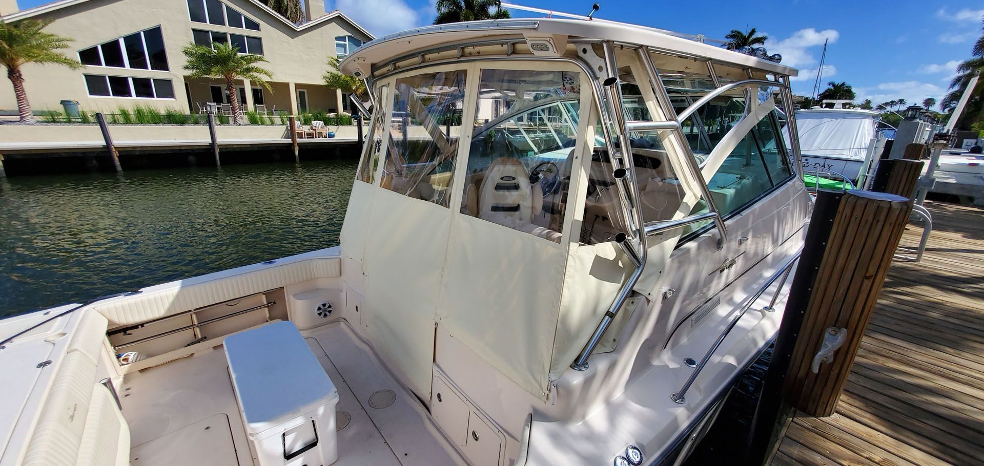 A beige motorboat docked in a canal with a canvas and plastic enclosure.
