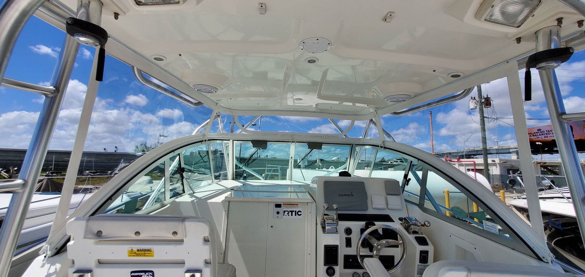 Interior view of a boat with a white dashboard, steering wheel, and windshield, blue sky visible.