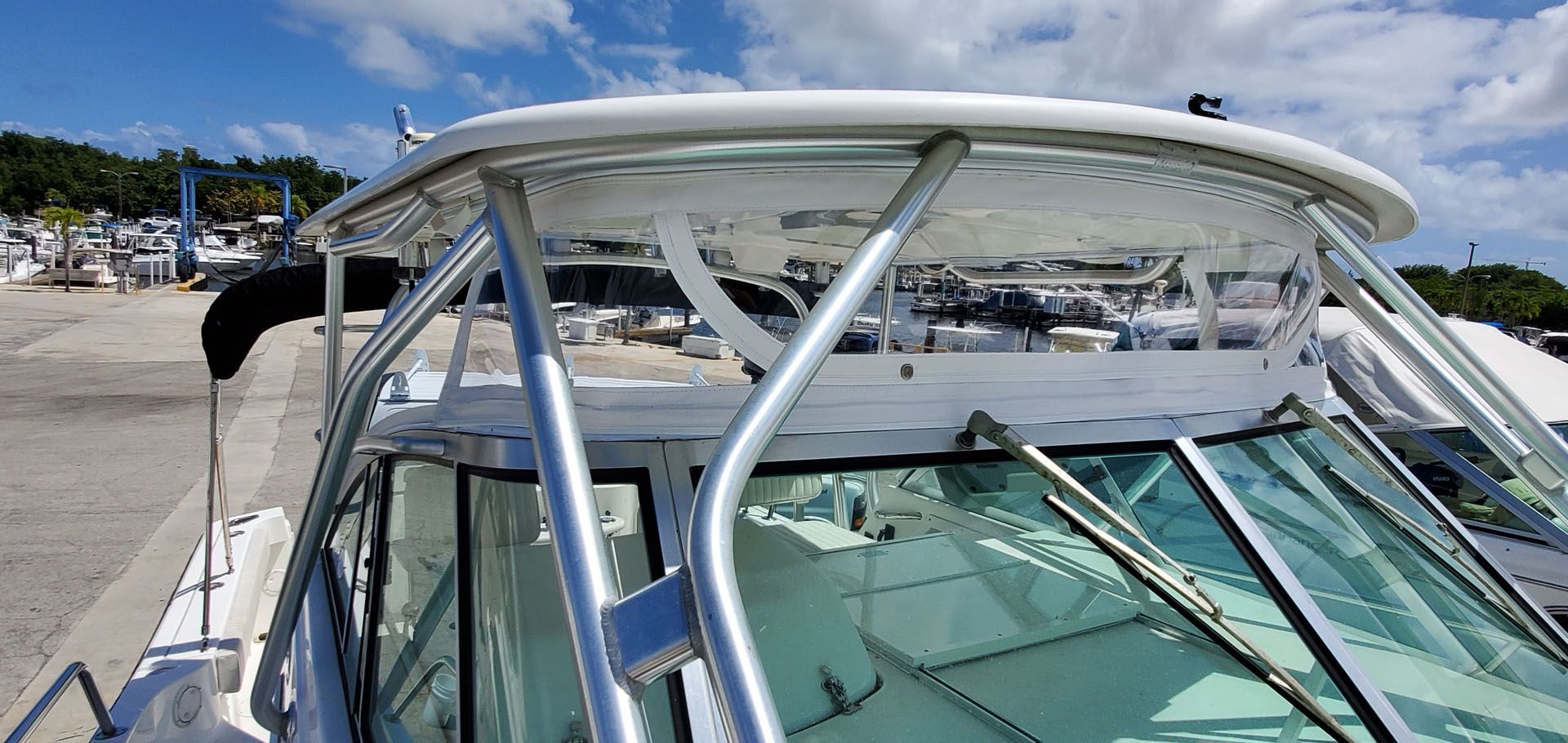 A boat's windshield, roof, and supporting metal frame, parked at a dock on a sunny day.