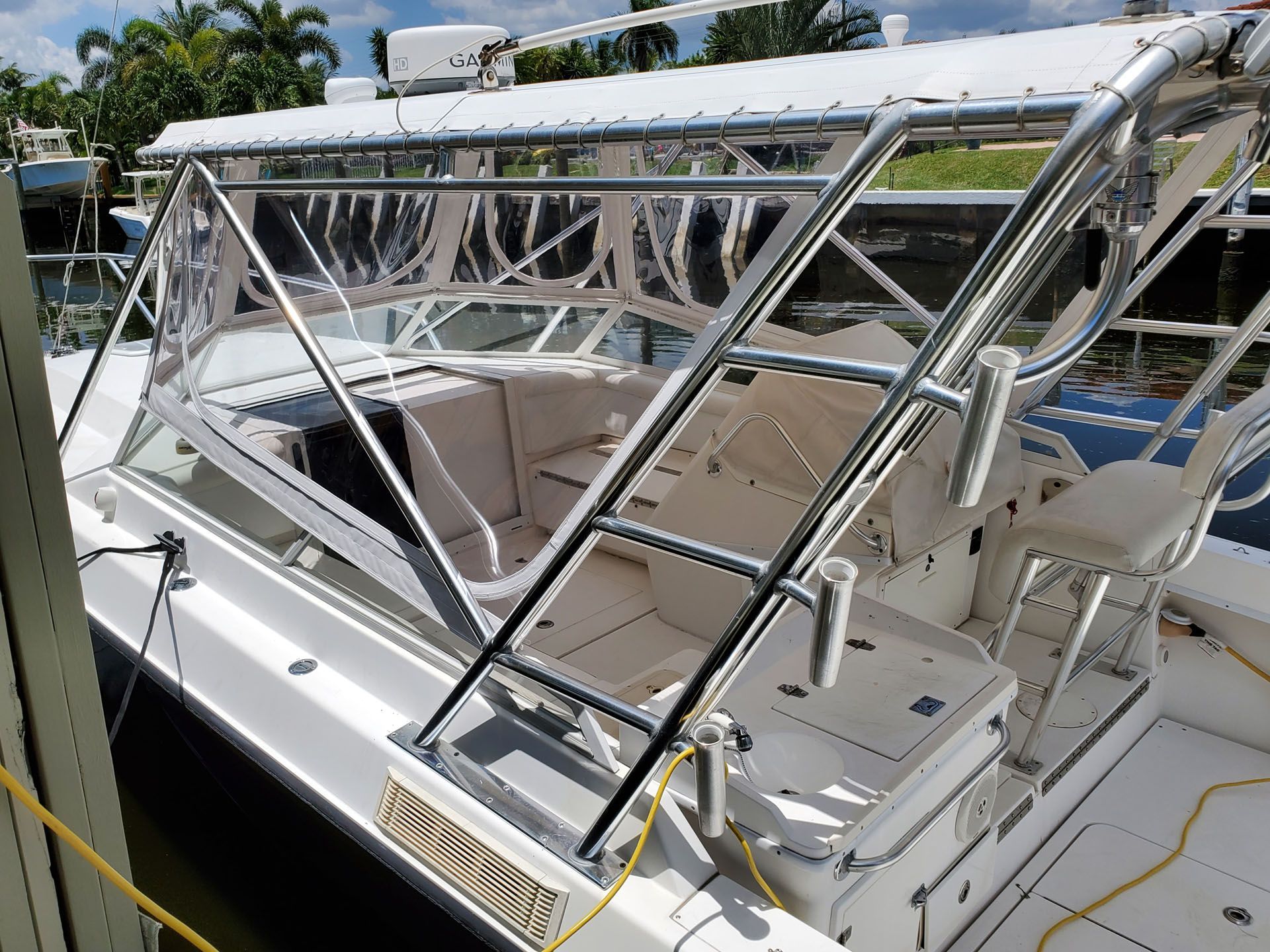 A white fishing boat with a clear enclosure and stainless steel railing docked at a marina.
