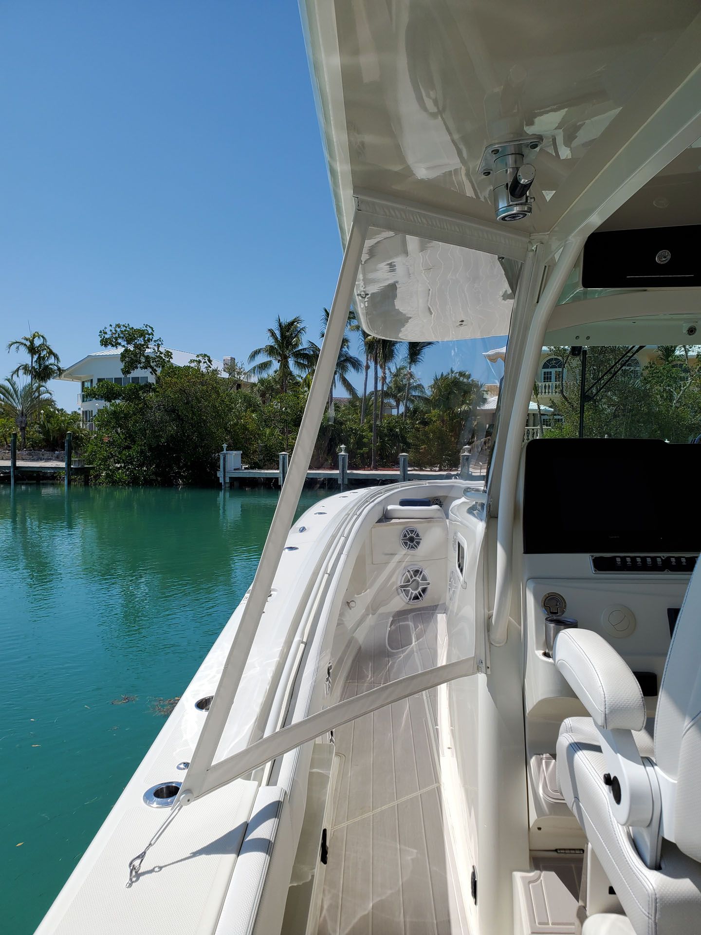 Boat interior with open side, view of water, palm trees, and houses on a sunny day.