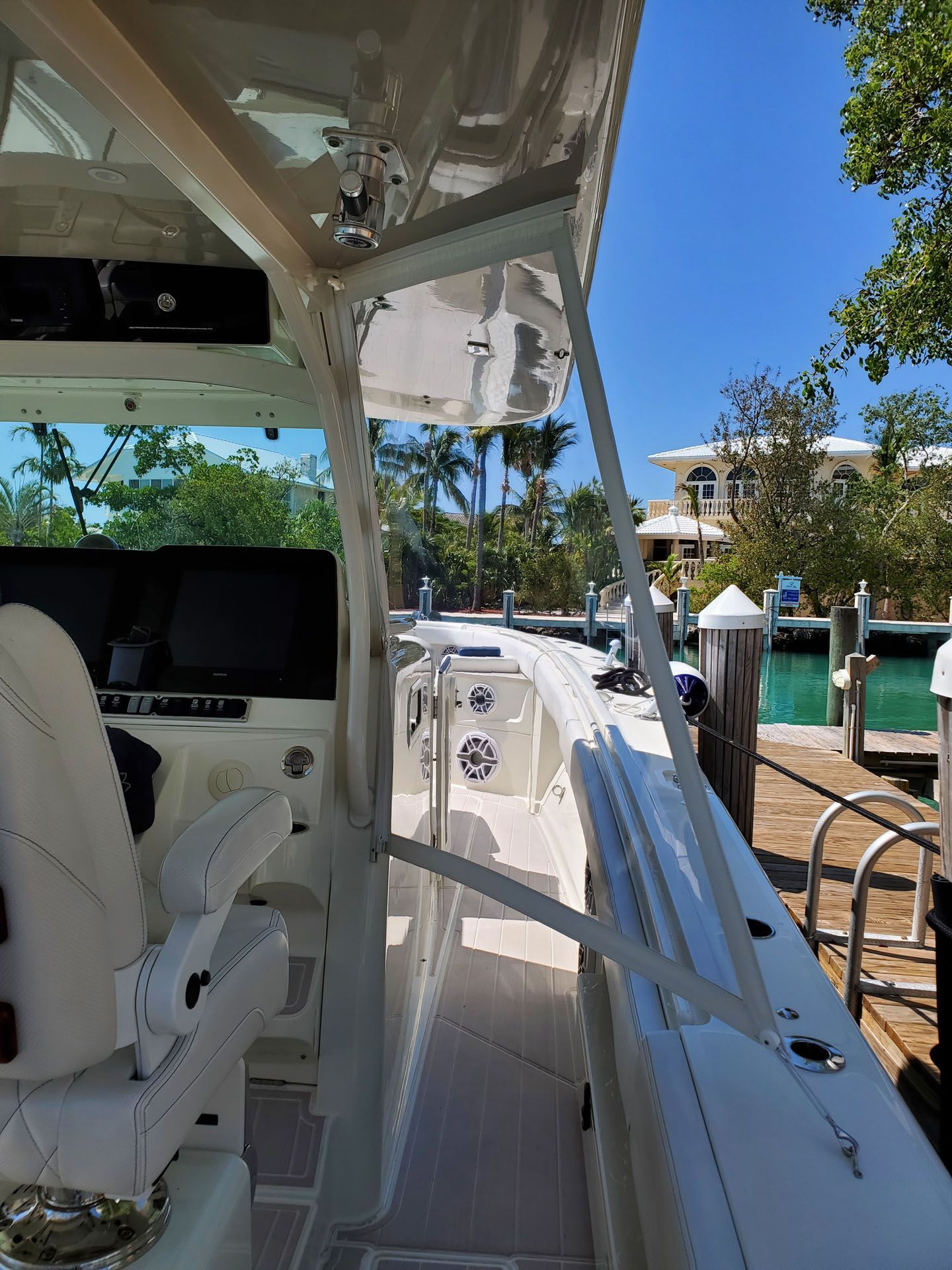 View from inside a white boat, looking out towards a dock. Bright blue sky and water visible.