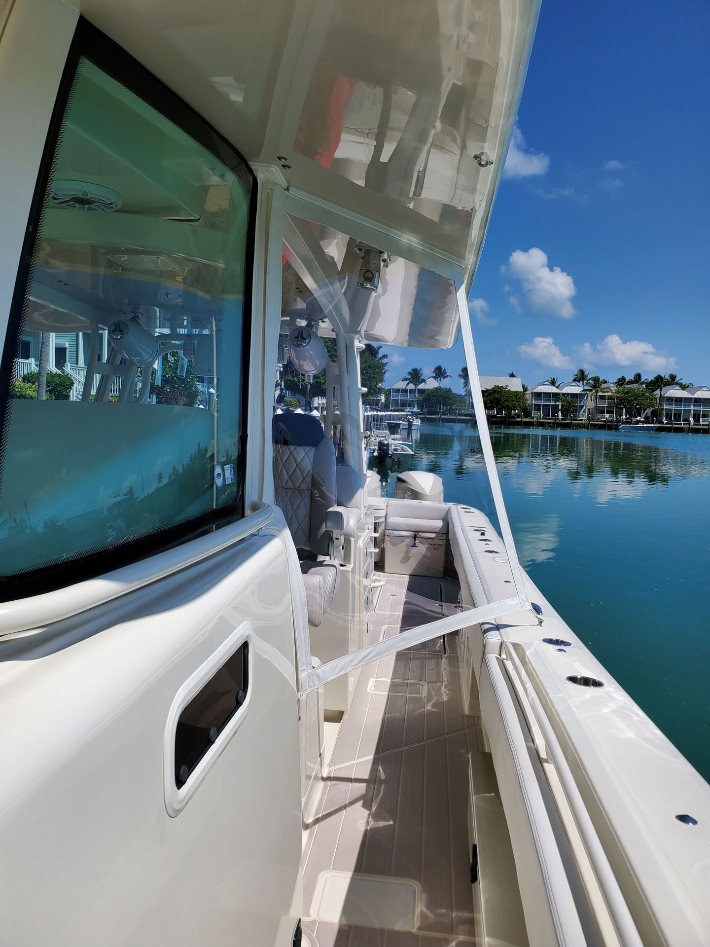 Side view of a boat on a sunny day, featuring a window and dockside view with buildings and water.