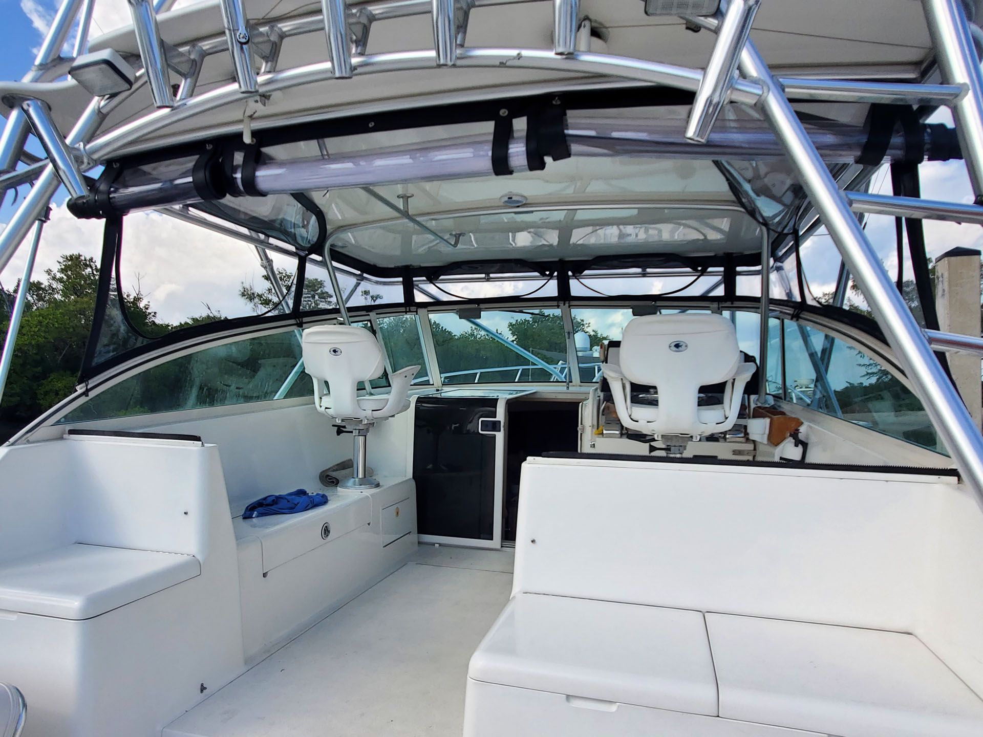 Interior view of a white fishing boat's helm with captain's chairs, windshield, and a hardtop.