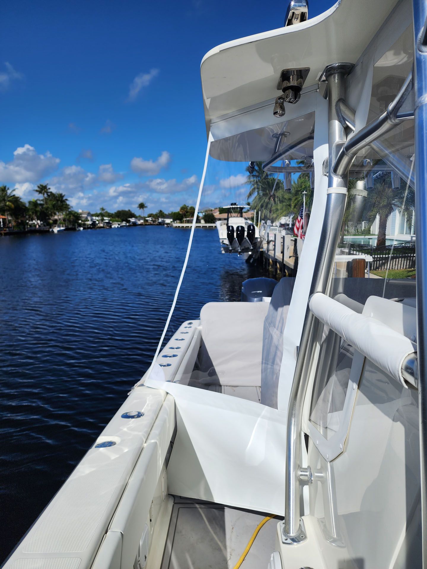 Boat docked on a canal; white boat with blue water and sky; trees and other boats in background.