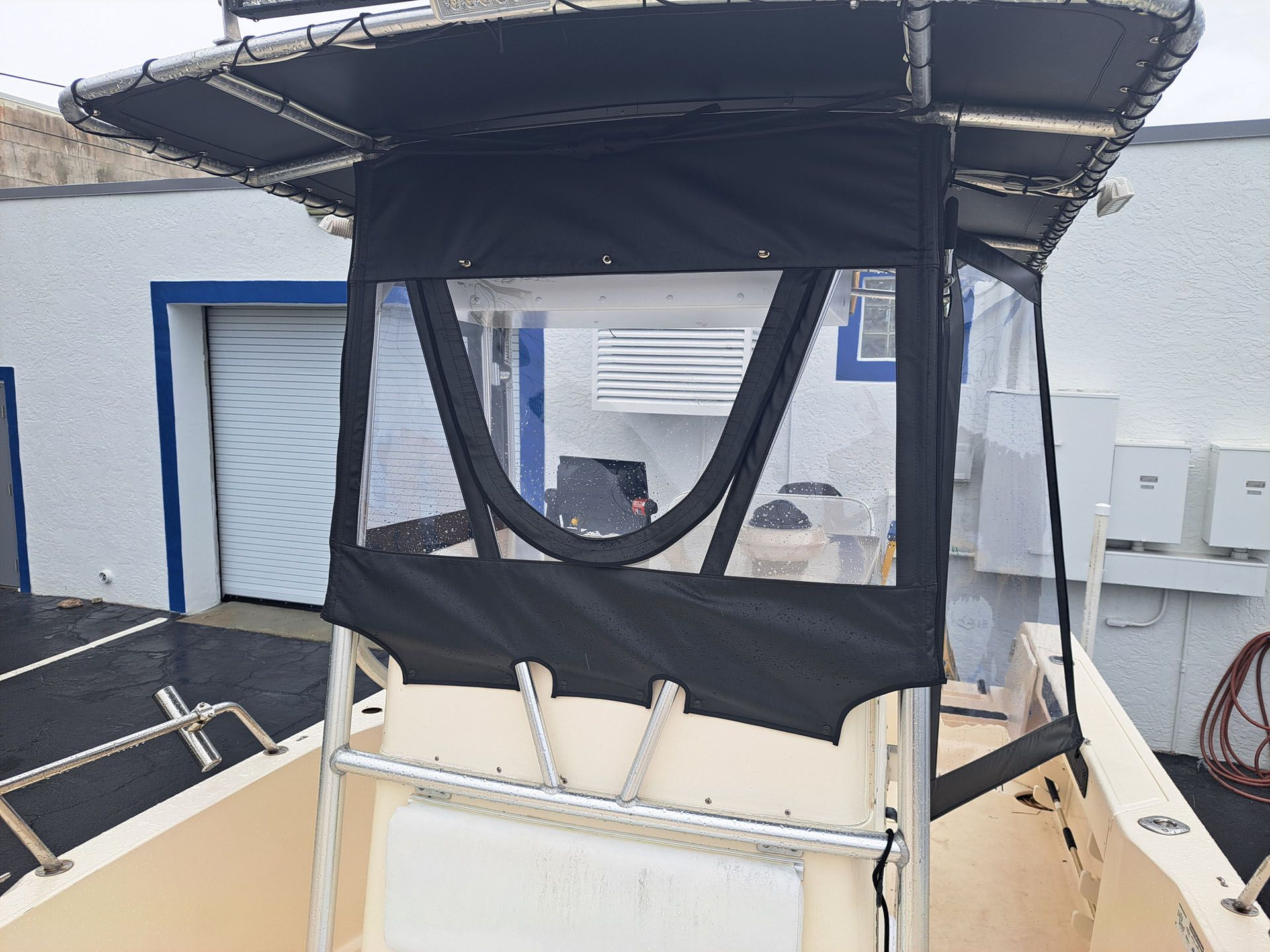 Black-canvassed boat center console with clear windscreen, under a metal frame and overhead canopy.