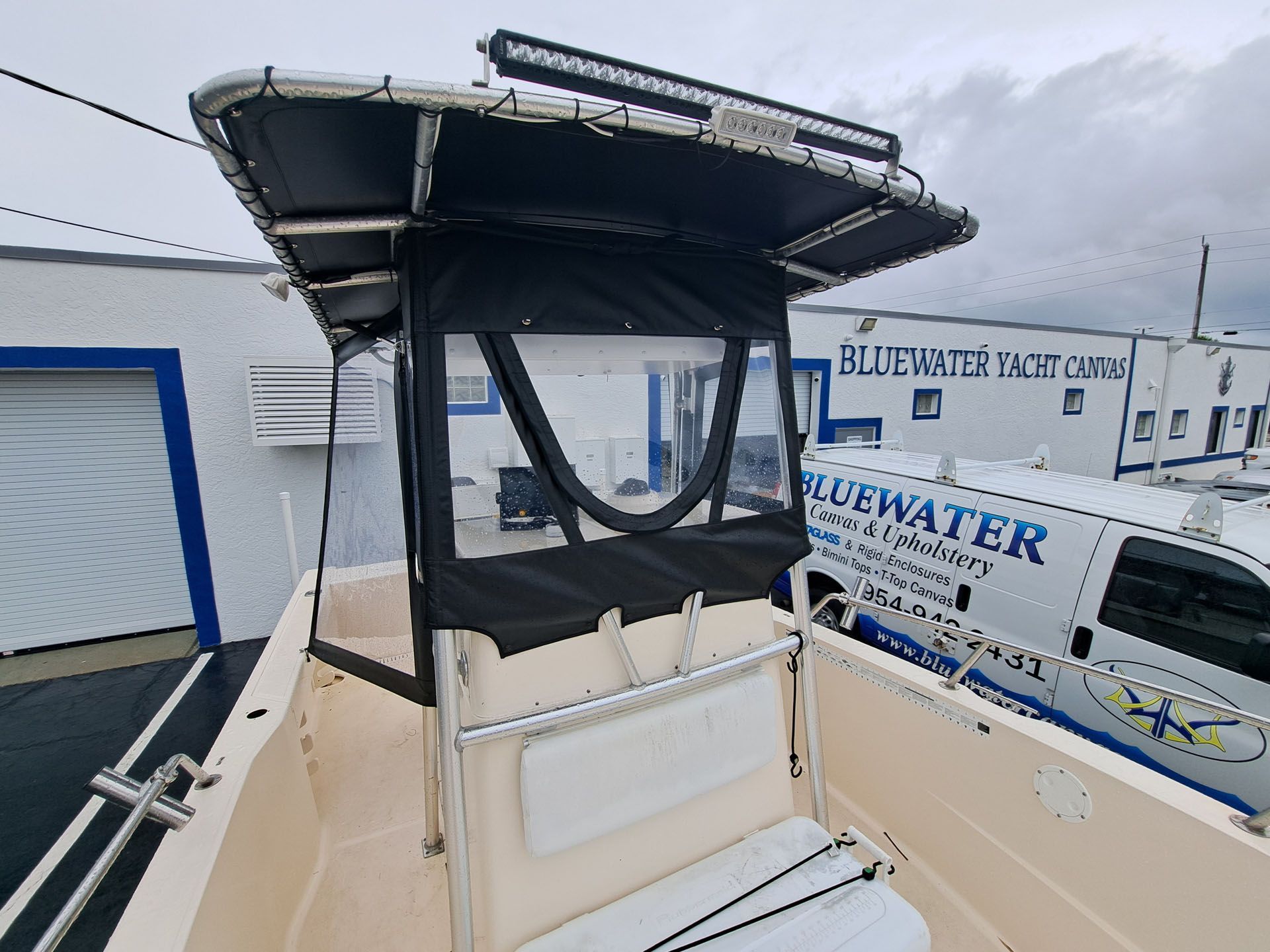 Boat cabin with black canvas, clear windows, and LED light bar, in front of a building.