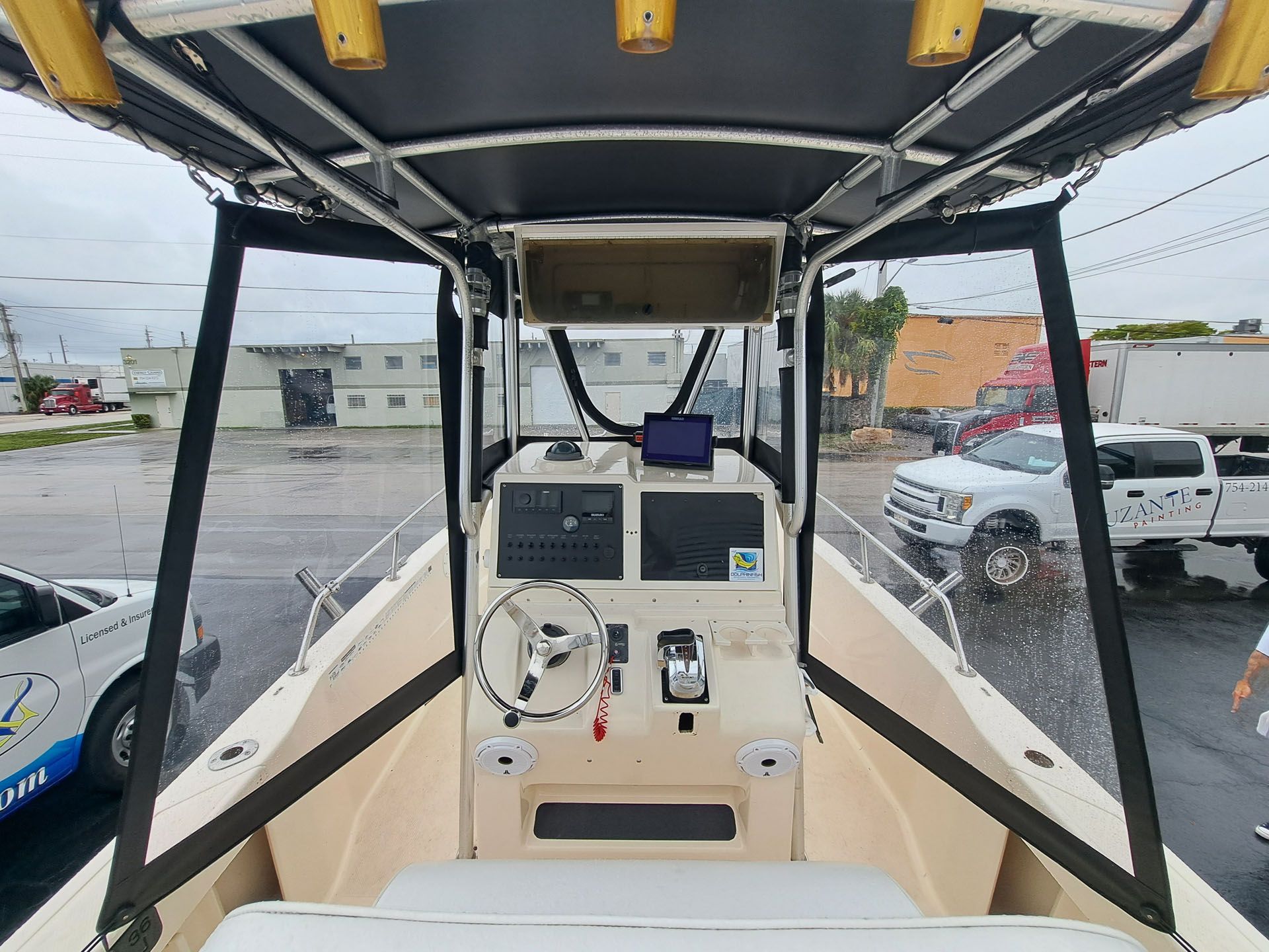 Interior view of a boat's helm station on an overcast day. Steering wheel, gauges, and windshield are visible.