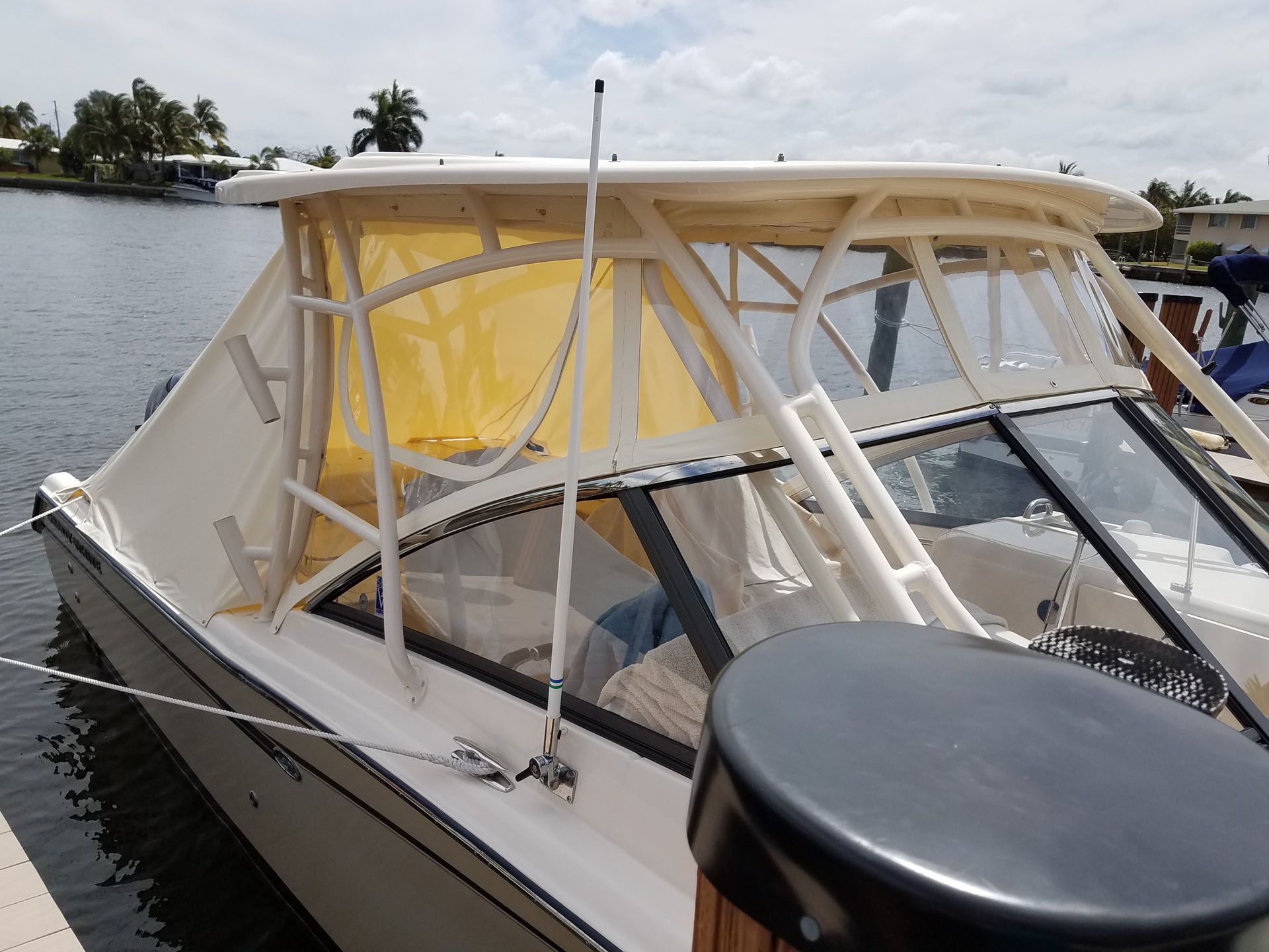 White boat with clear and yellow canvas enclosure on a dock, canal in background.
