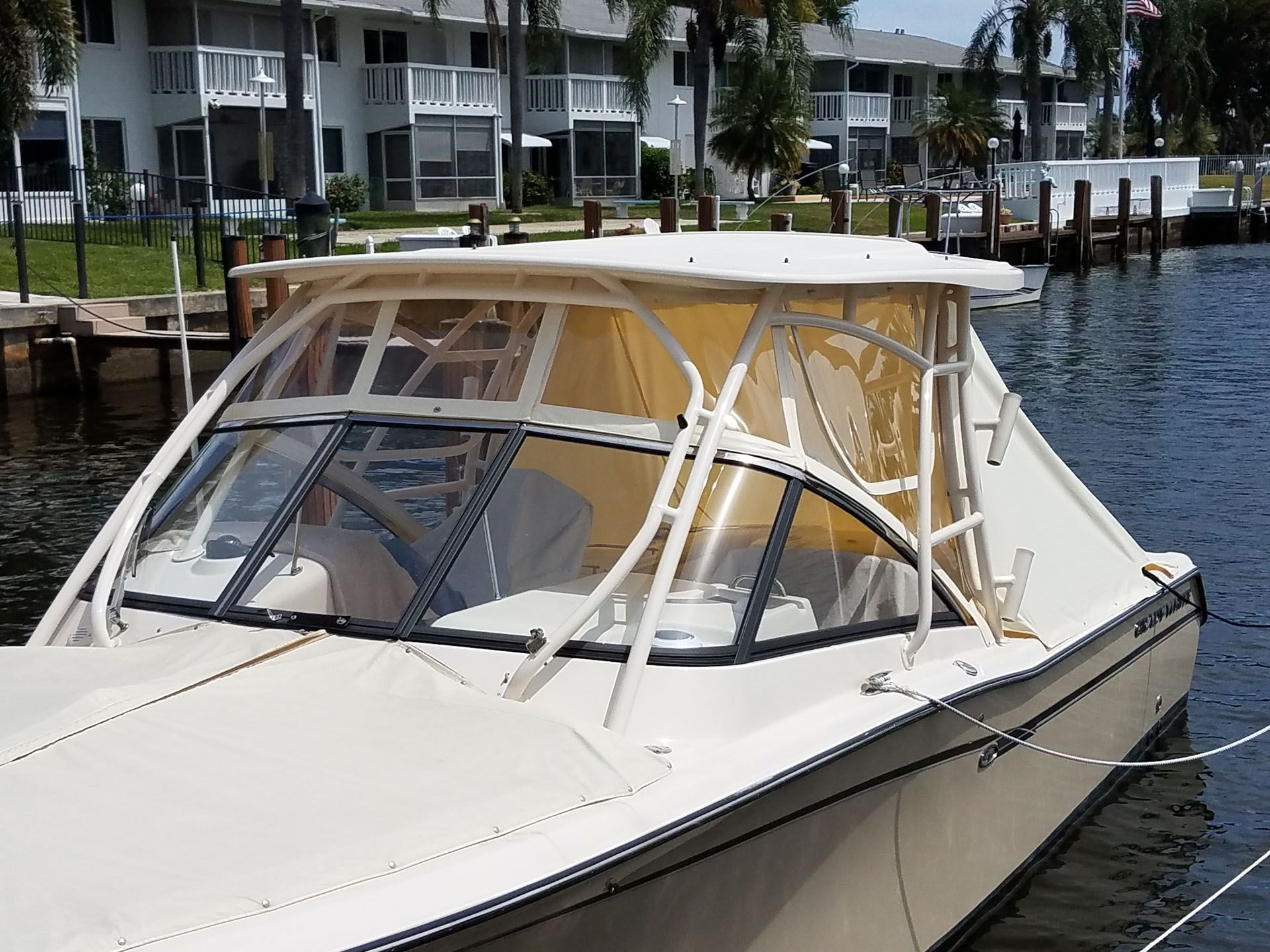 Boat with beige canvas enclosure, docked near waterfront condos.