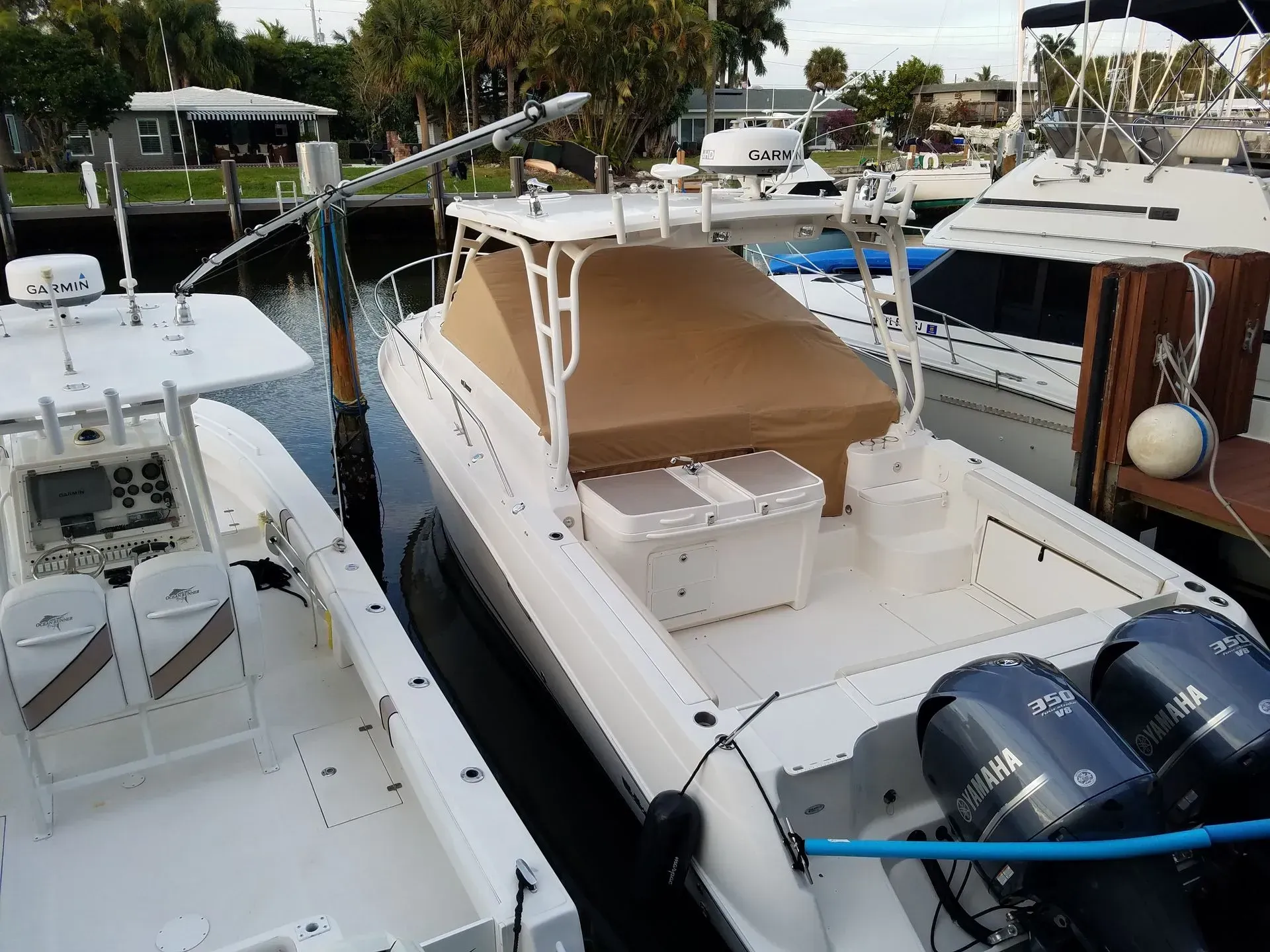 White boats docked in a waterway. One has a tan canopy and two outboard motors.