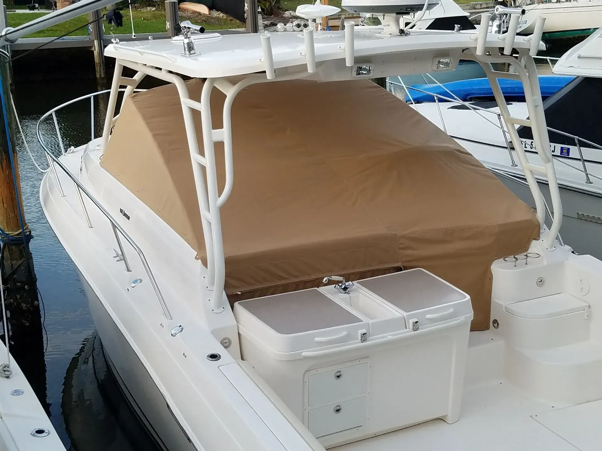Tan covered boat with white frame on a dock, sunny day.