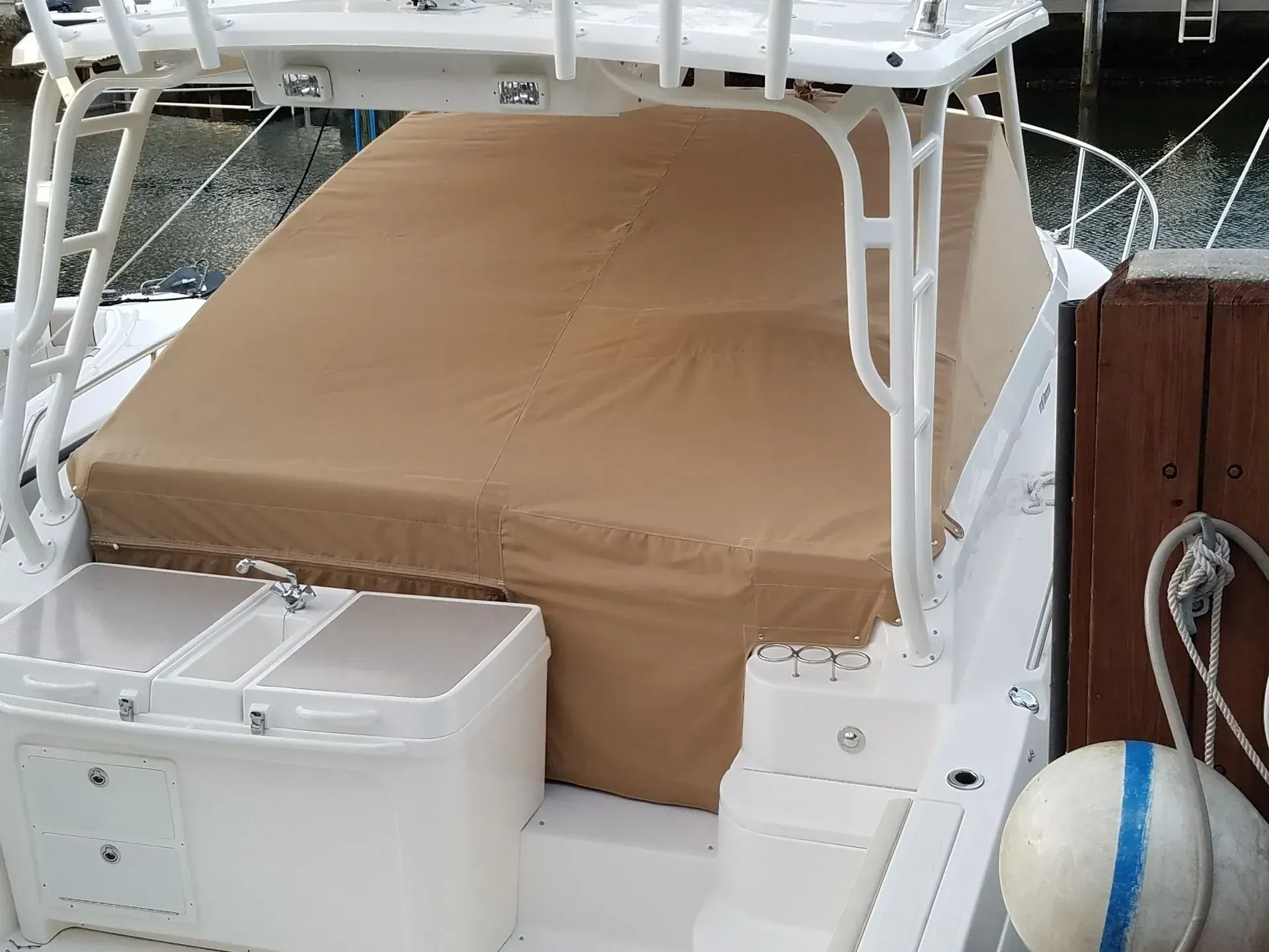 Tan canvas enclosure on a white boat, covering back area. White metal frame, three white bins.