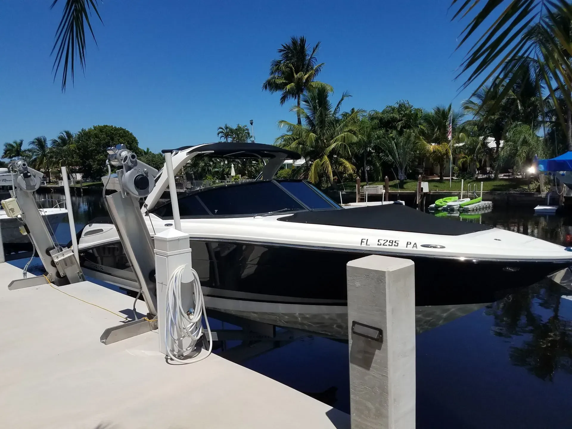Black and white motorboat docked in a canal under a bright blue sky. Palm trees in the background.
