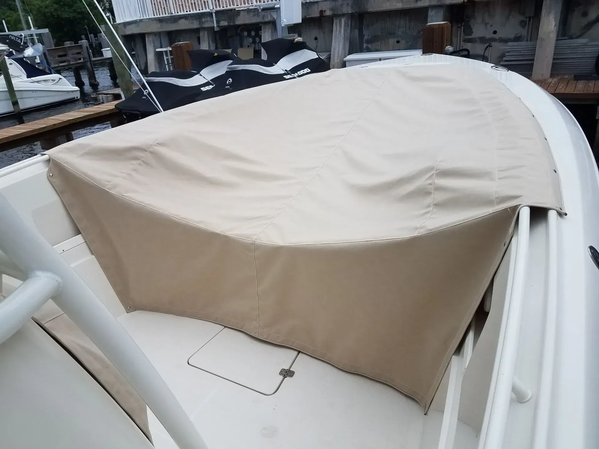 Beige boat cover on a white boat, protecting the front area near a dock.