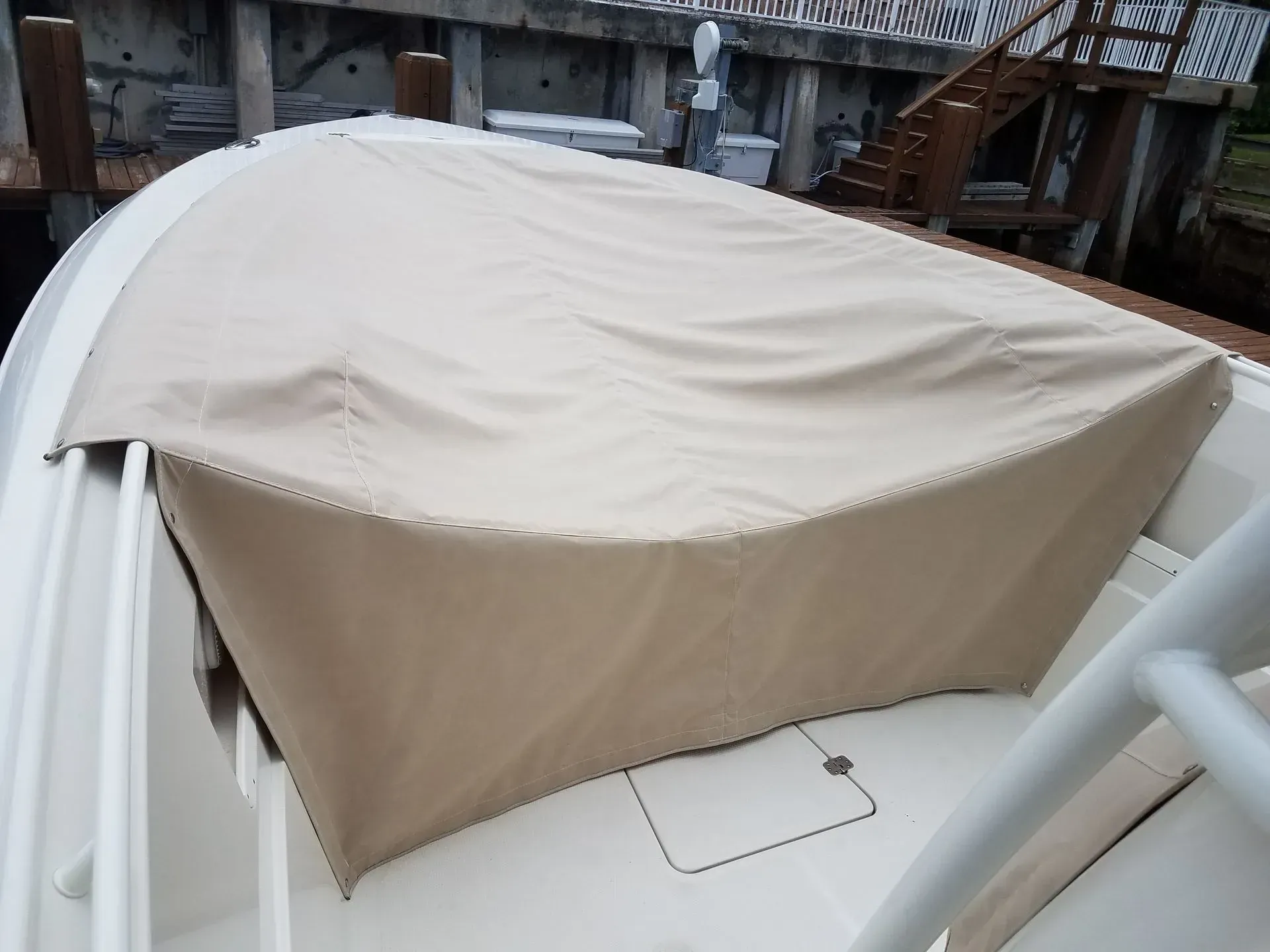 Tan boat cover on a white boat deck near a wooden dock and stairs.