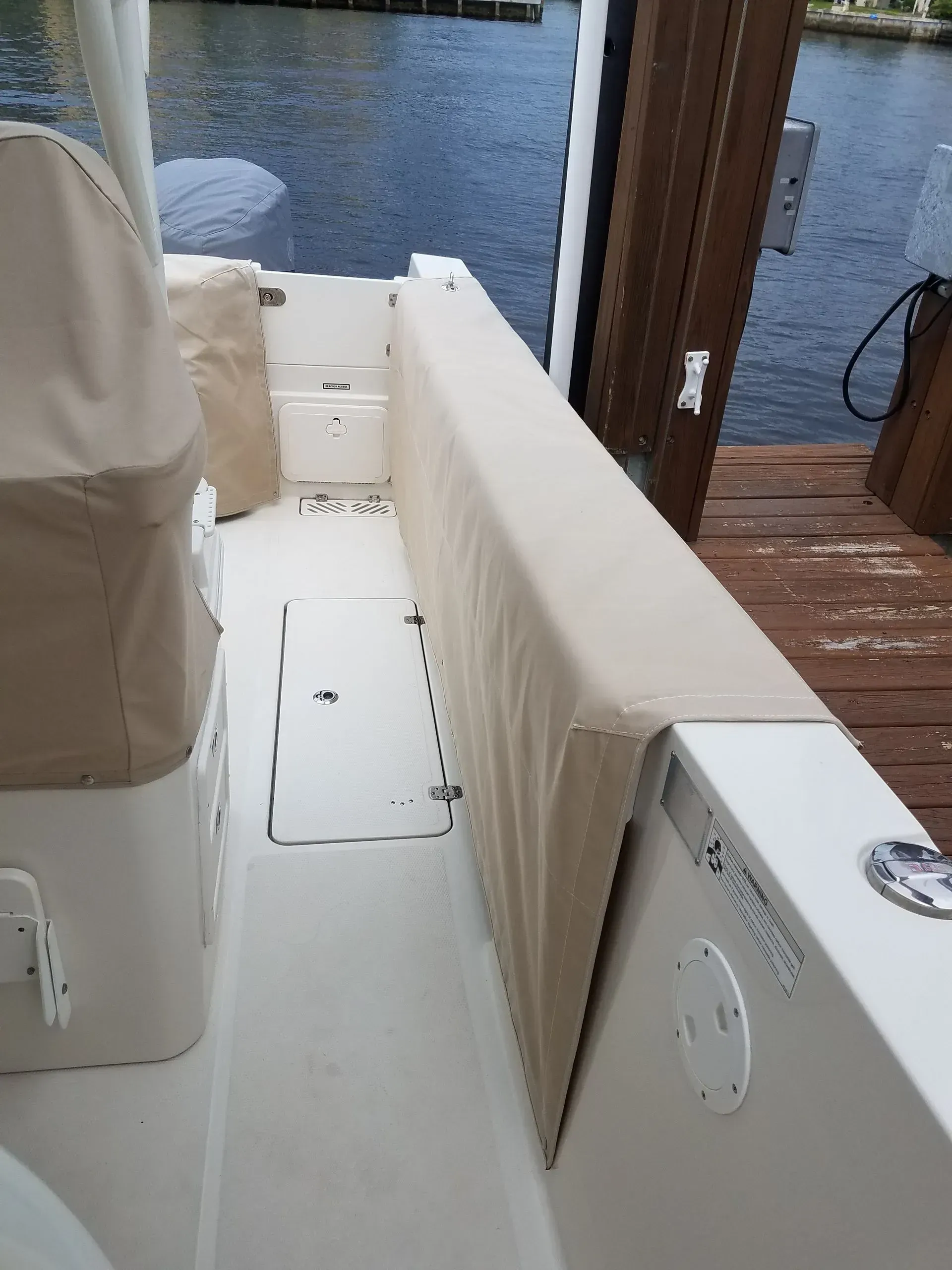 Boat's interior with tan cushions along a white walkway beside a wooden dock.