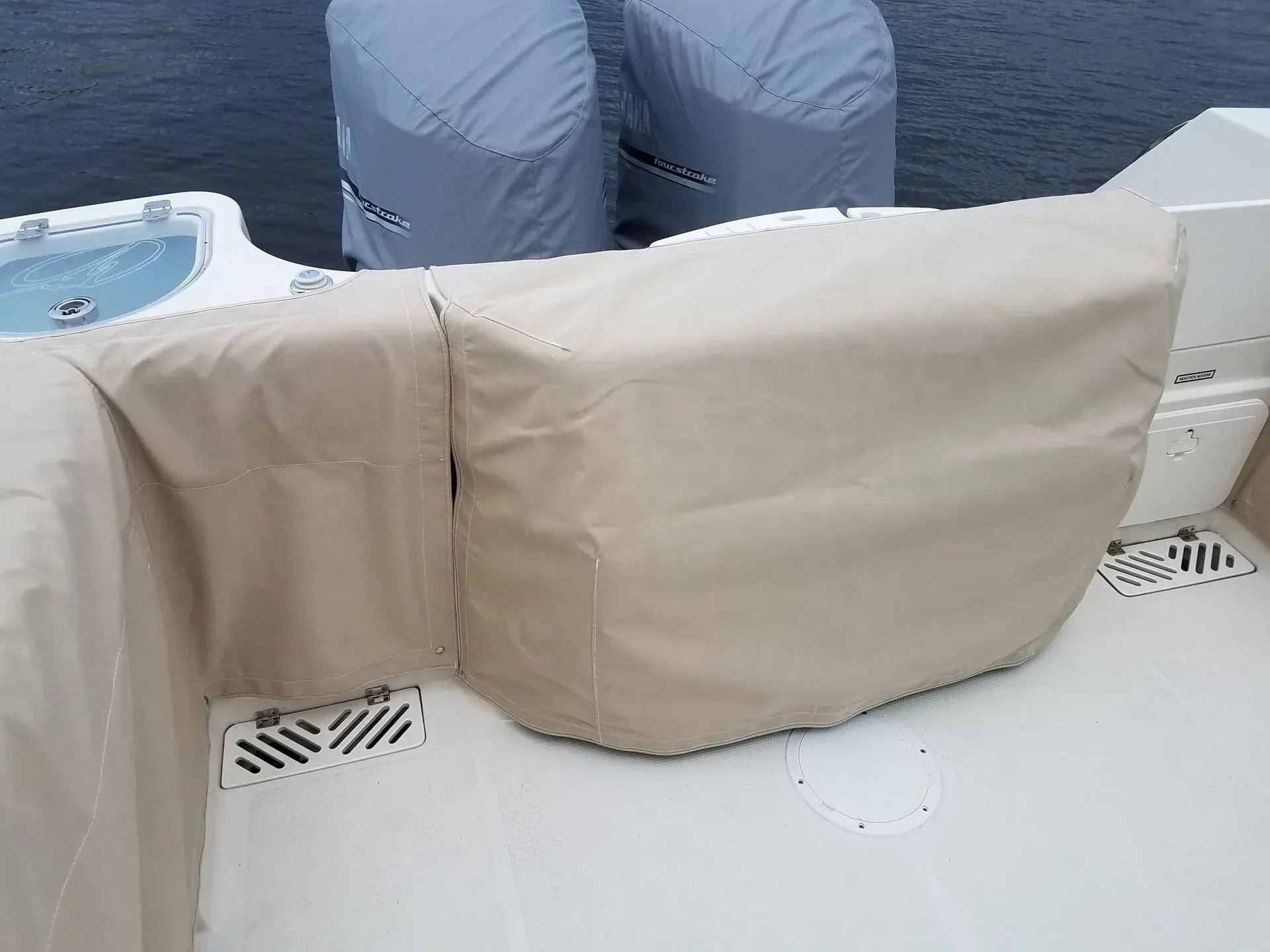 A tan boat's rear interior with protective covers on seating and engines, near the water.