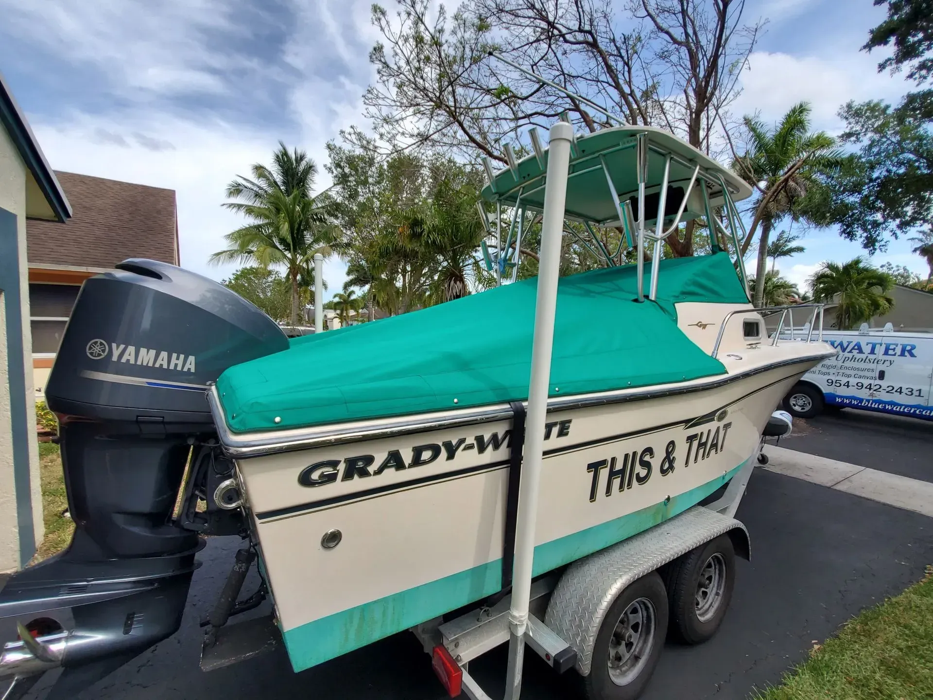 A teal covered Grady-White boat on a trailer, with a Yamaha engine, parked outside, under a bright sky.
