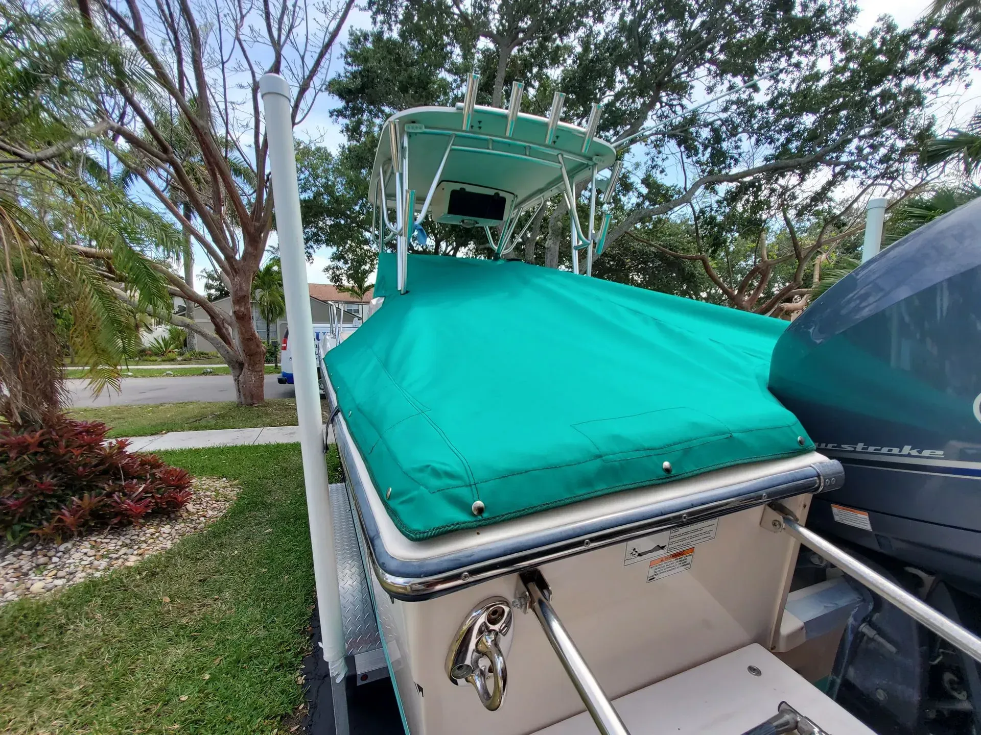 A boat covered in green tarp; parked on a trailer in a yard.
