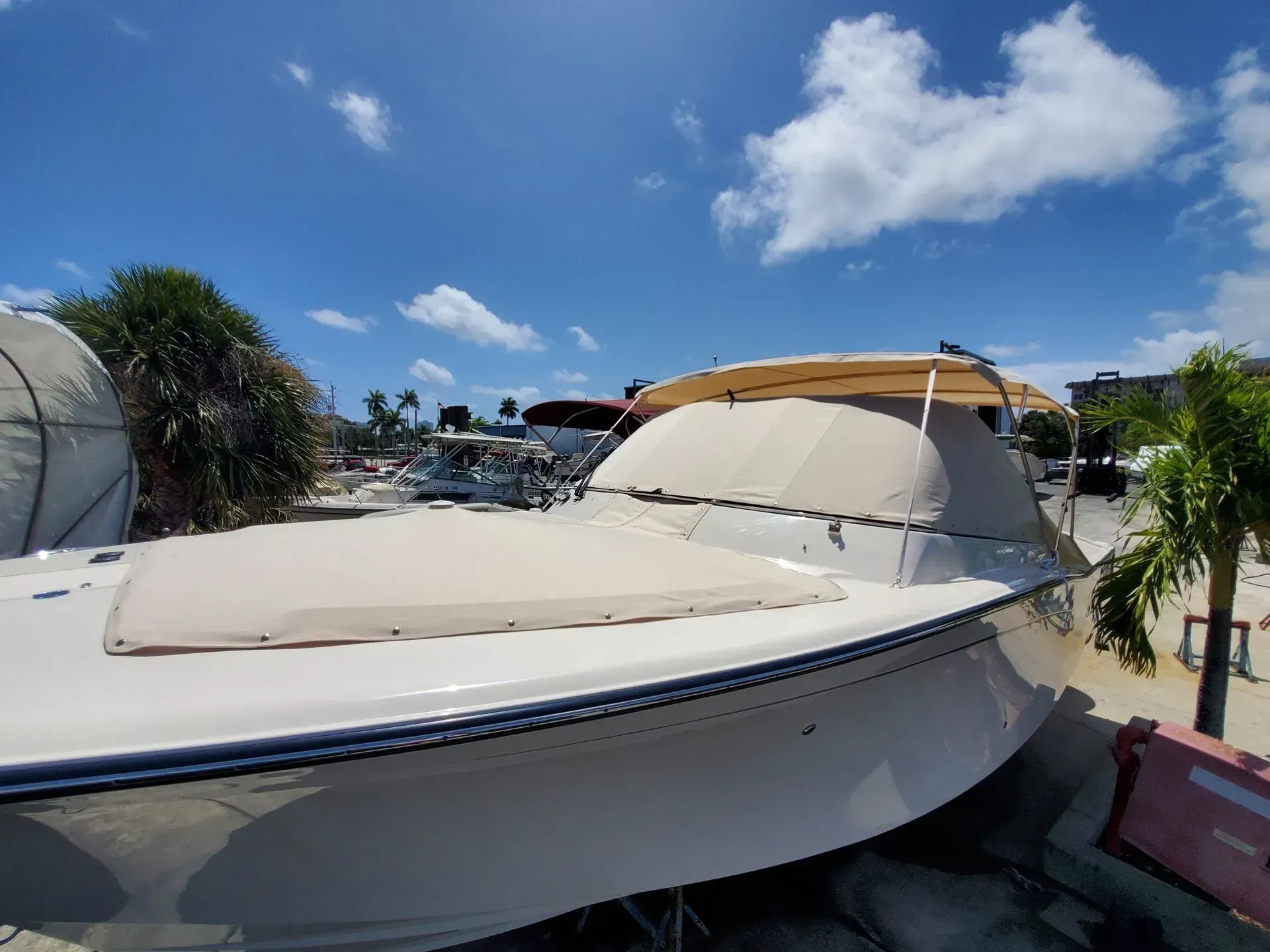 Boat covered in beige fabric, docked outdoors under a blue sky with clouds.