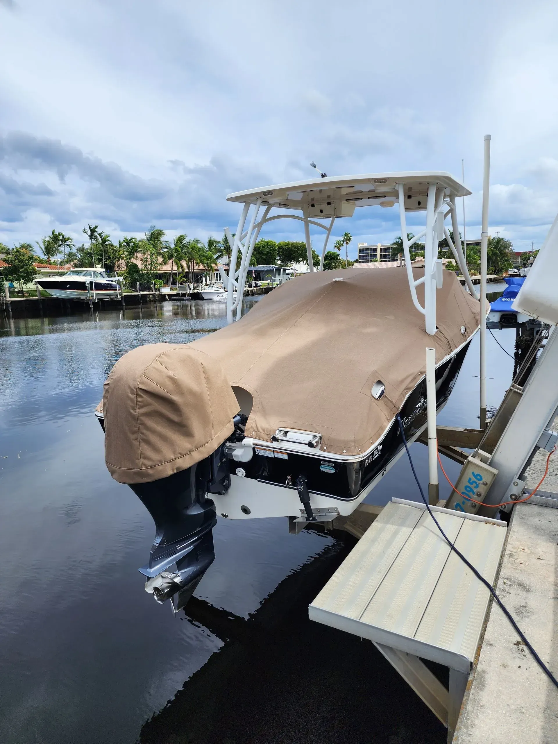 Boat docked on a lift, covered with a tan tarp, under a white canopy; waterfront setting.