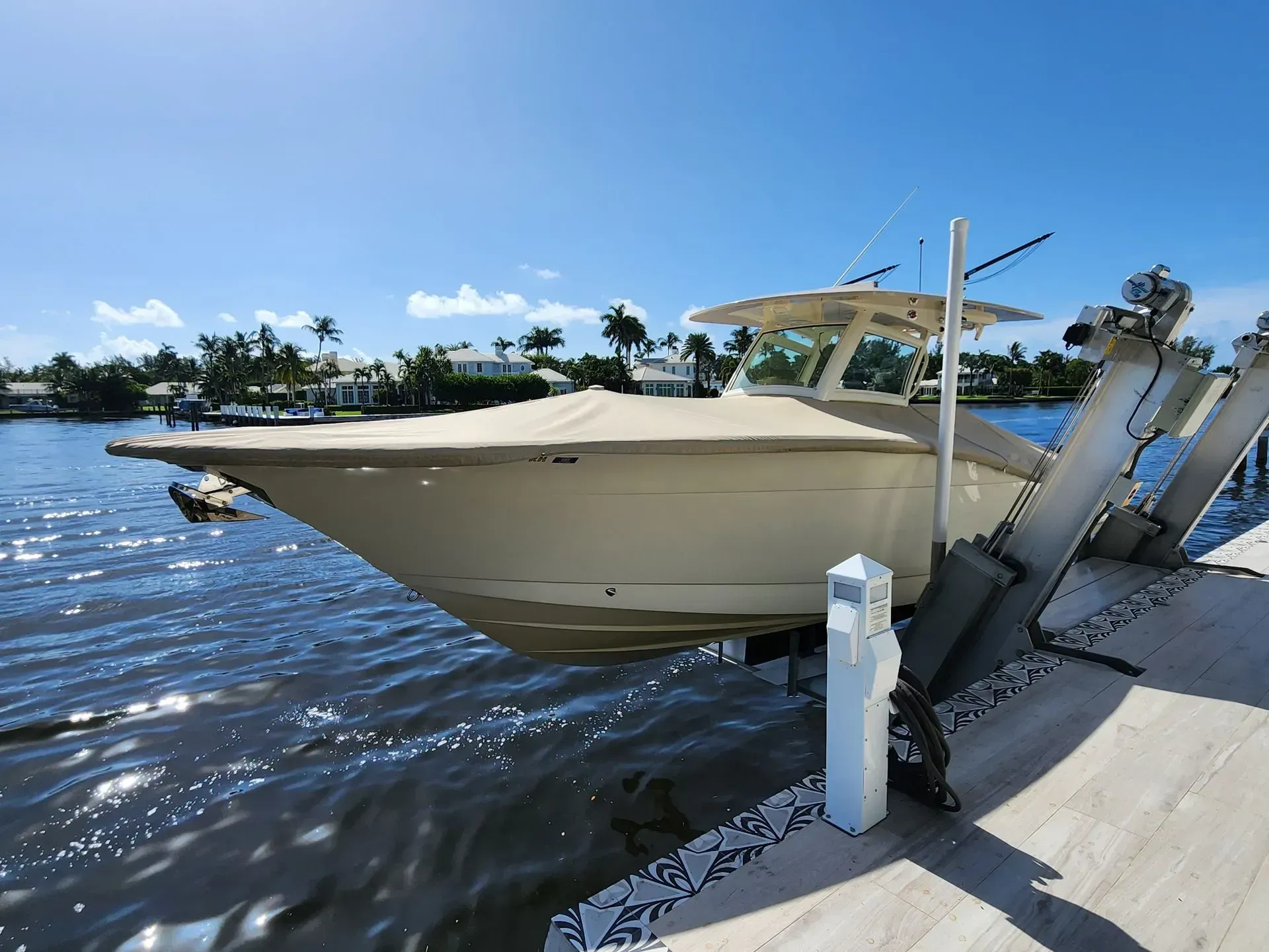 Boat with tan cover on lift in water, palm trees in background on sunny day.