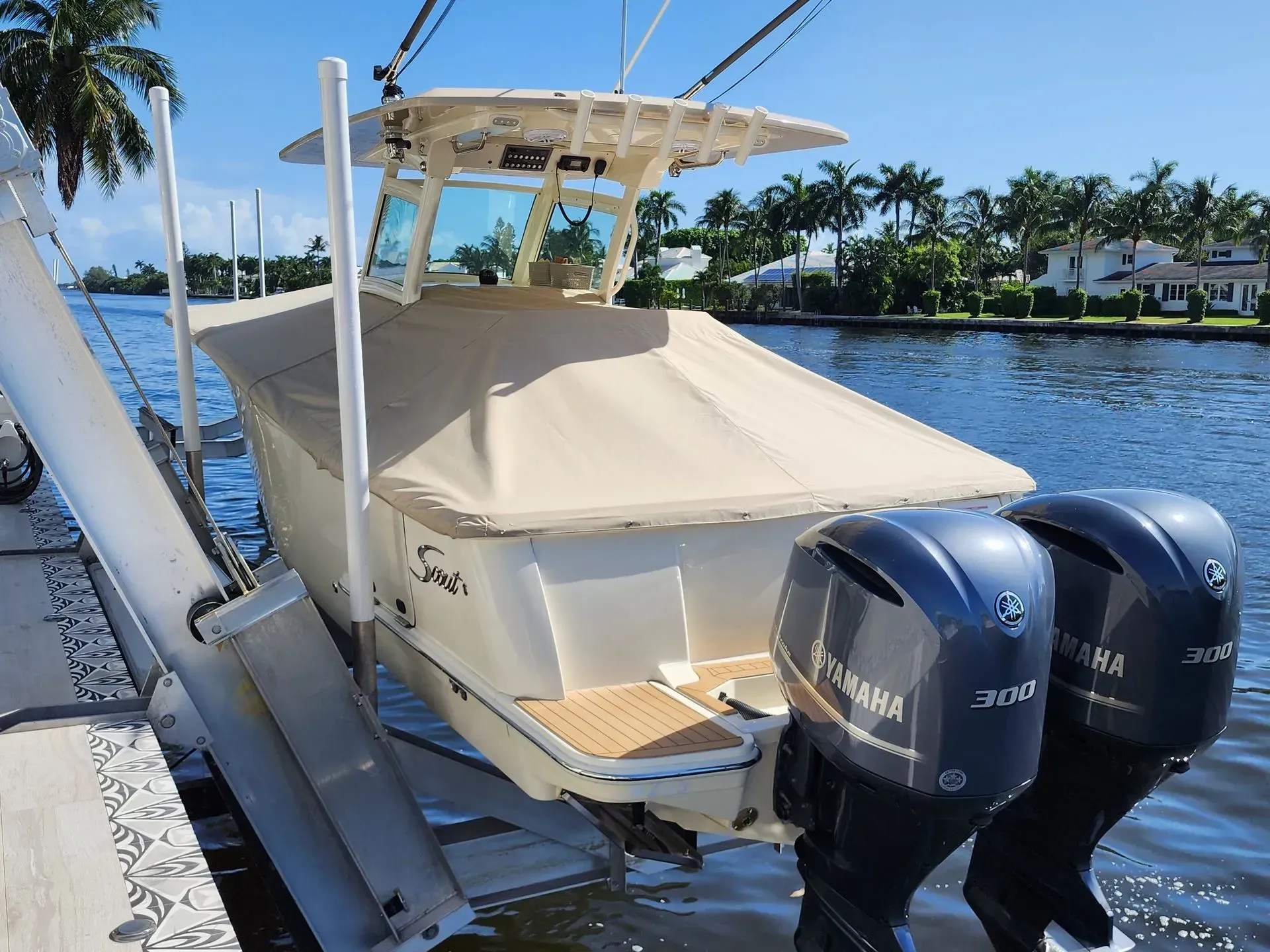 A tan and white motorboat on a boat lift, with twin Yamaha engines and a beige cover.