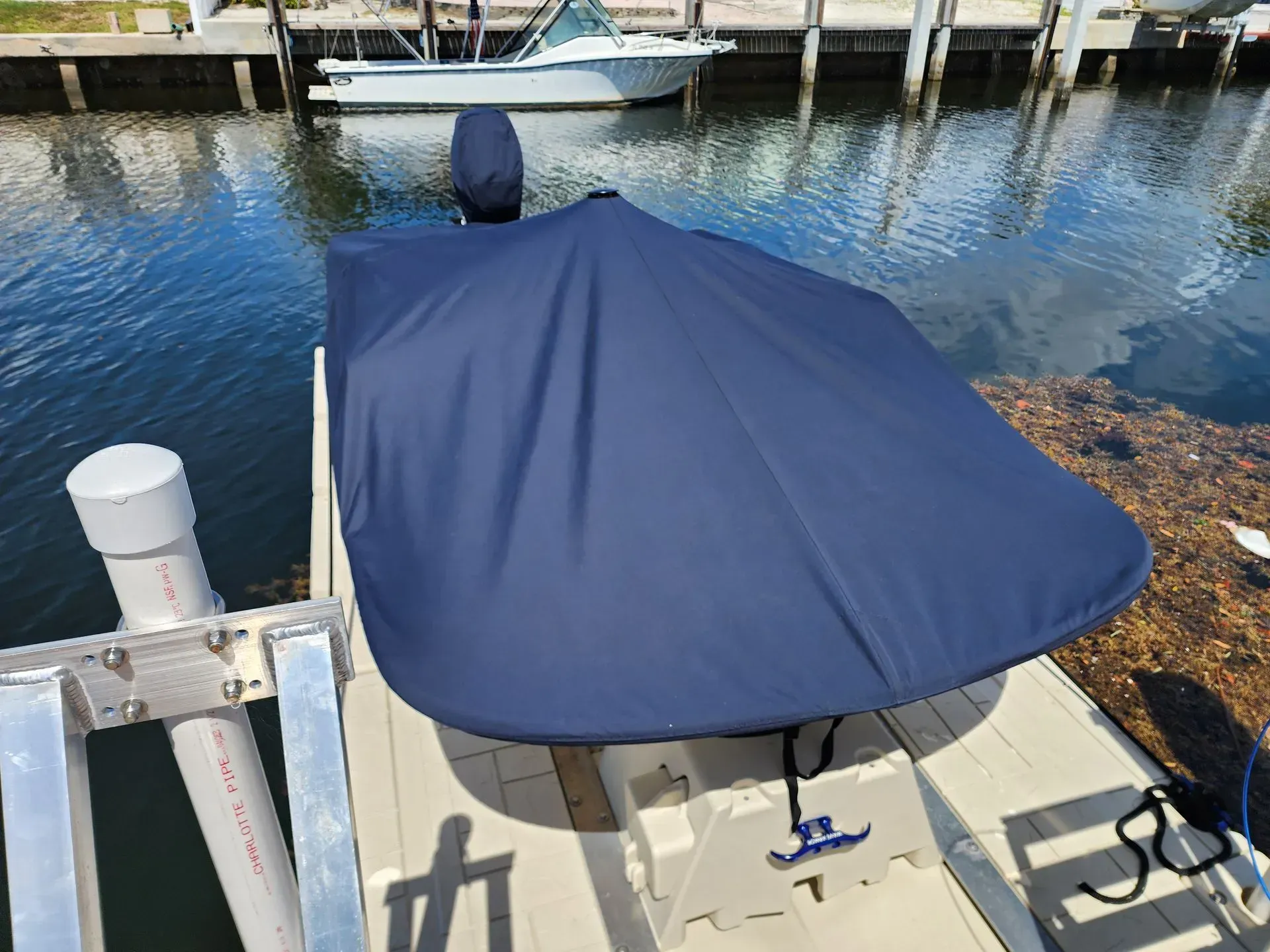 Blue boat cover on a small boat docked at a pier; water and other boats in the background.