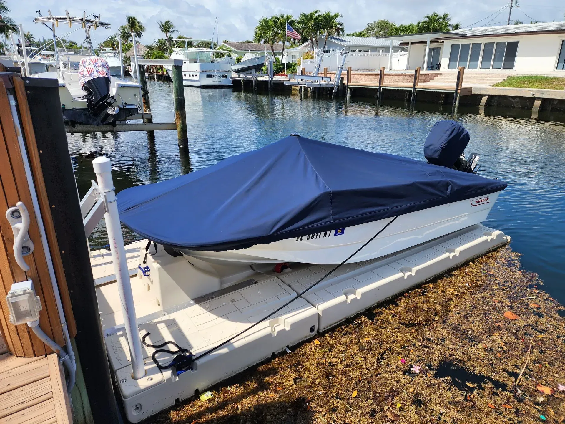 Small white boat with blue cover on a floating dock in a canal.