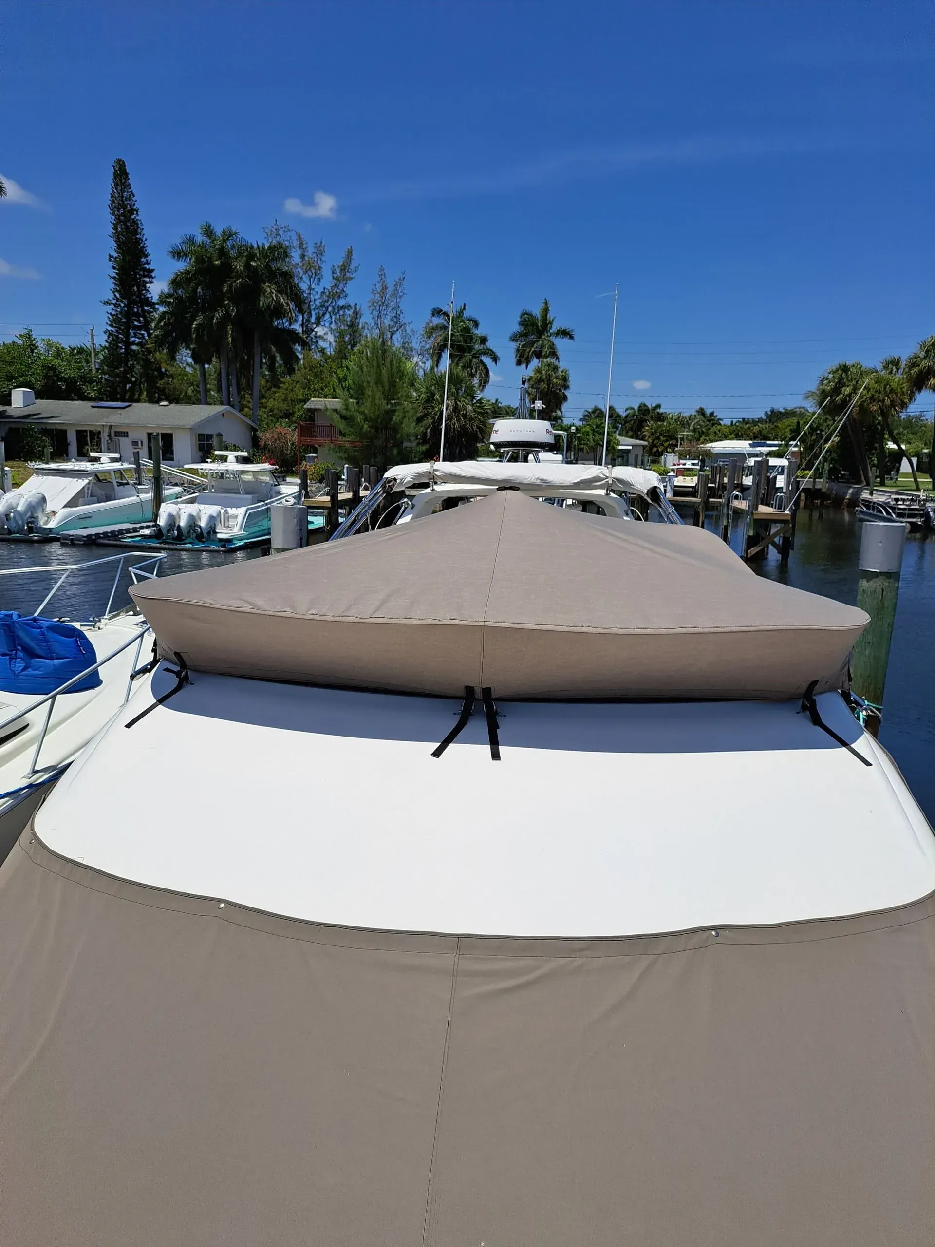 A beige boat cover on a white boat deck, docked in a canal on a sunny day.
