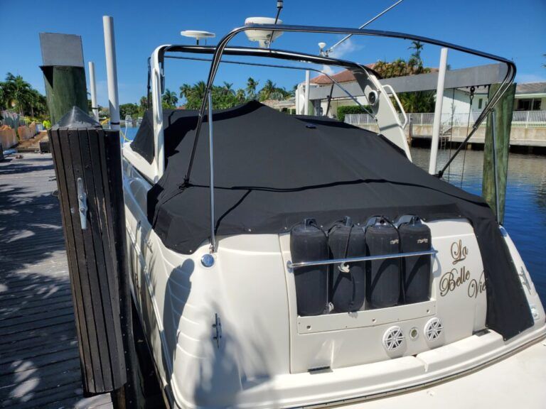 A white boat with a black cover is docked at a dock