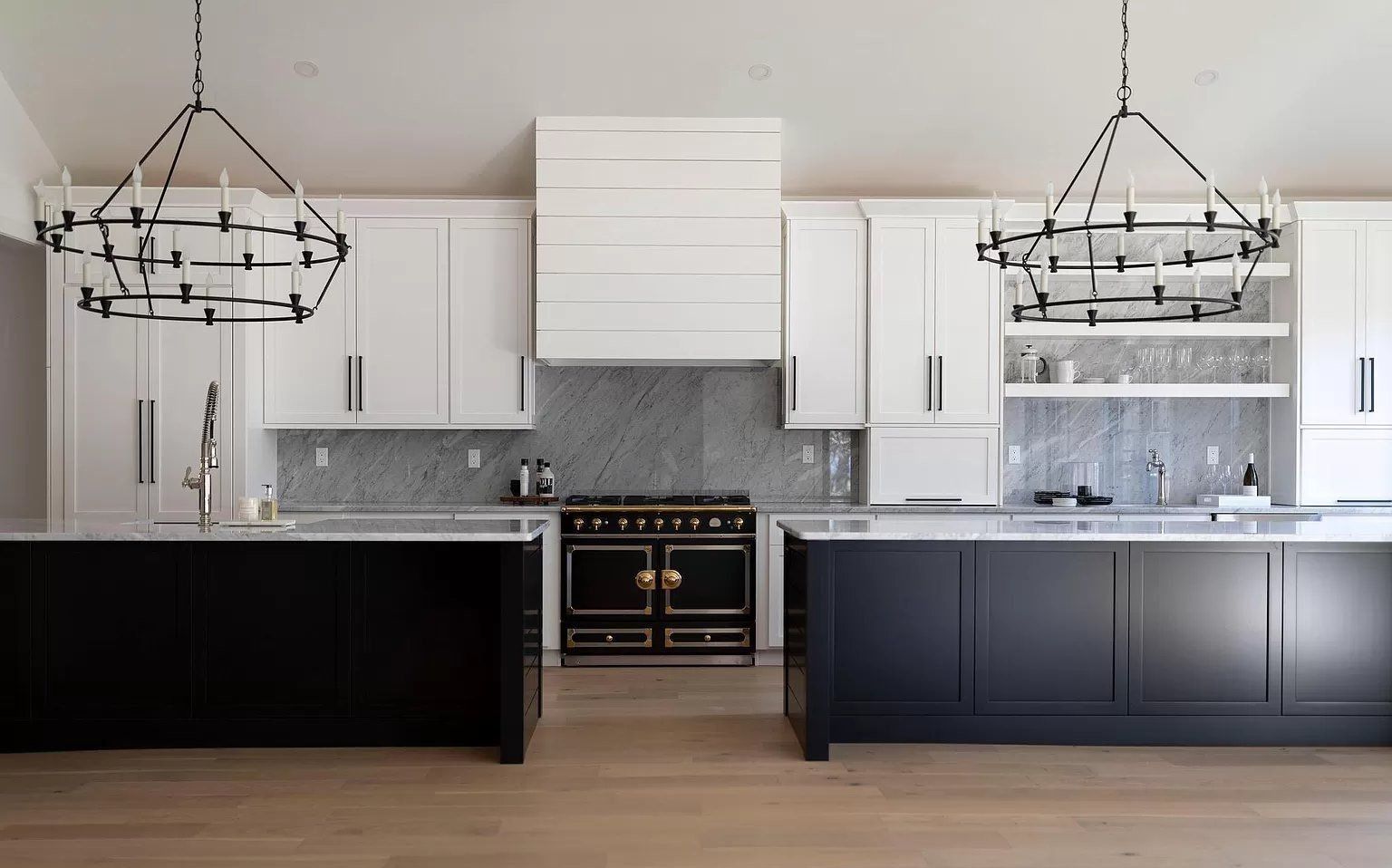 Modern kitchen with white cabinets, black lower cabinets, marble backsplash, and two black chandeliers
